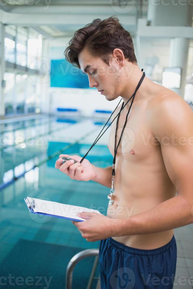 instrutor de natação segurando cronômetro e prancheta à beira da piscina foto