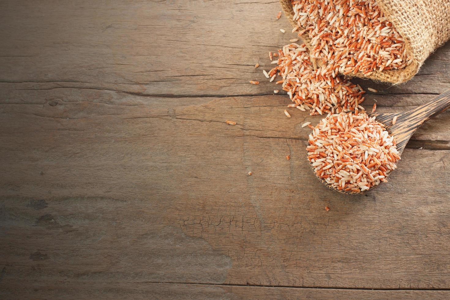 comida tailandesa de cereais - vista superior do arroz orgânico vermelho, arroz integral na colher de pau e saco deitado na mesa de madeira com espaço de cópia foto