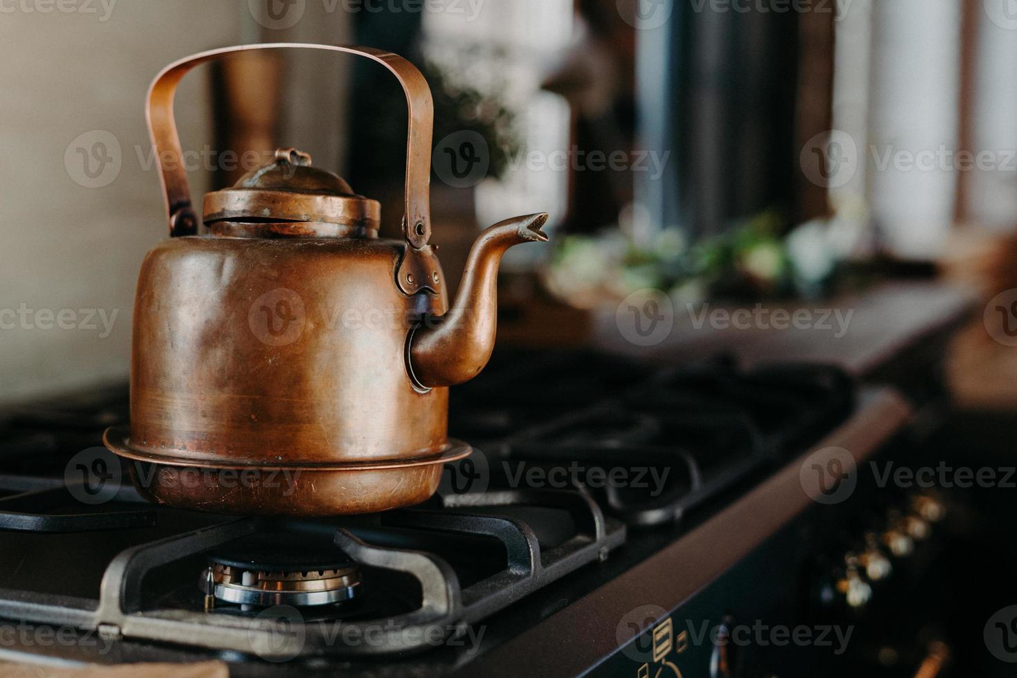 chaleira de bronze na cozinha moderna. antigo bule vintage no fogão a gás. preparando o chá. chaleira de alumínio. luz do dia ensolarado da janela. foto