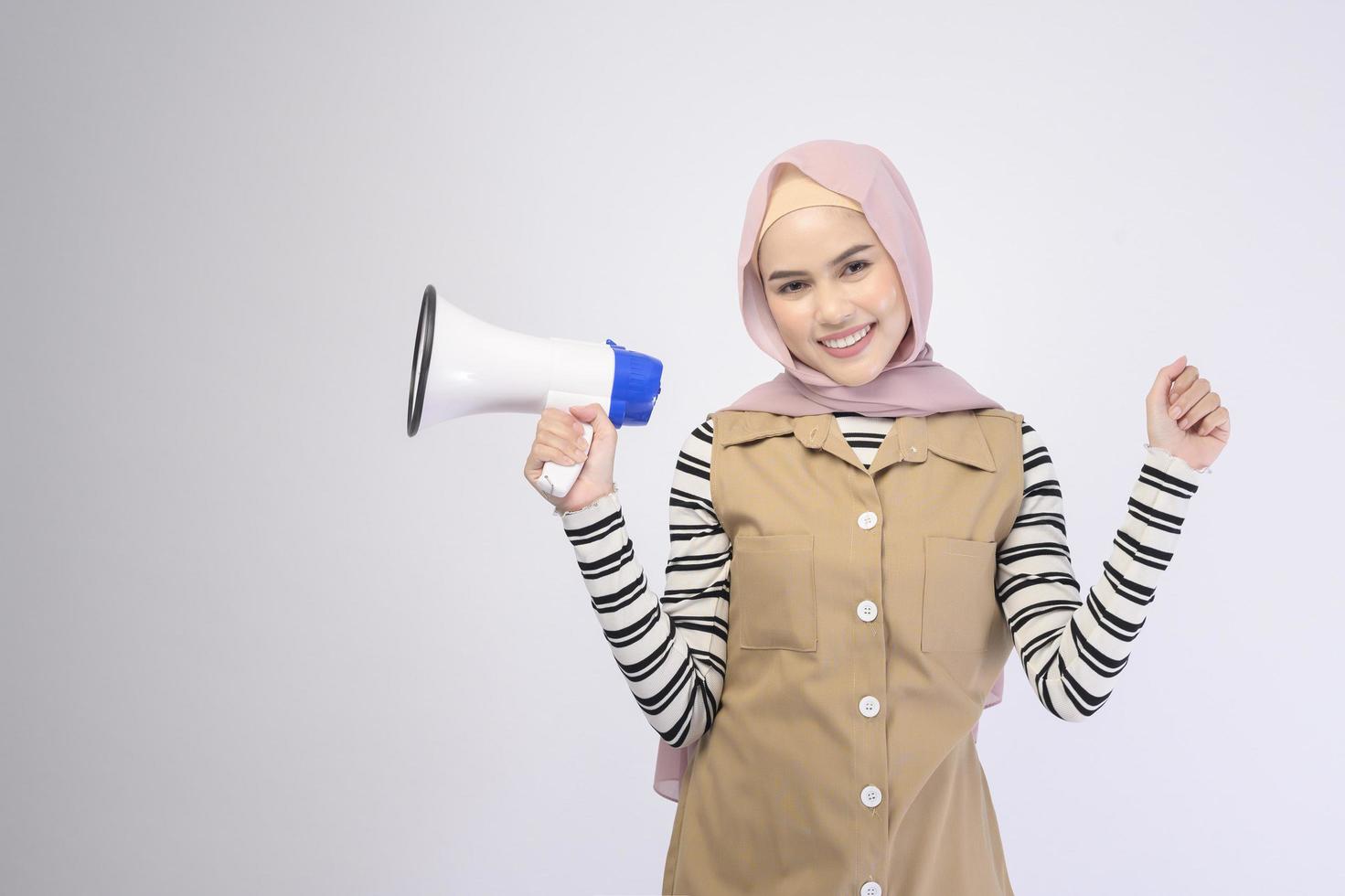 feliz mulher muçulmana está anunciando com megafone em fundo branco foto