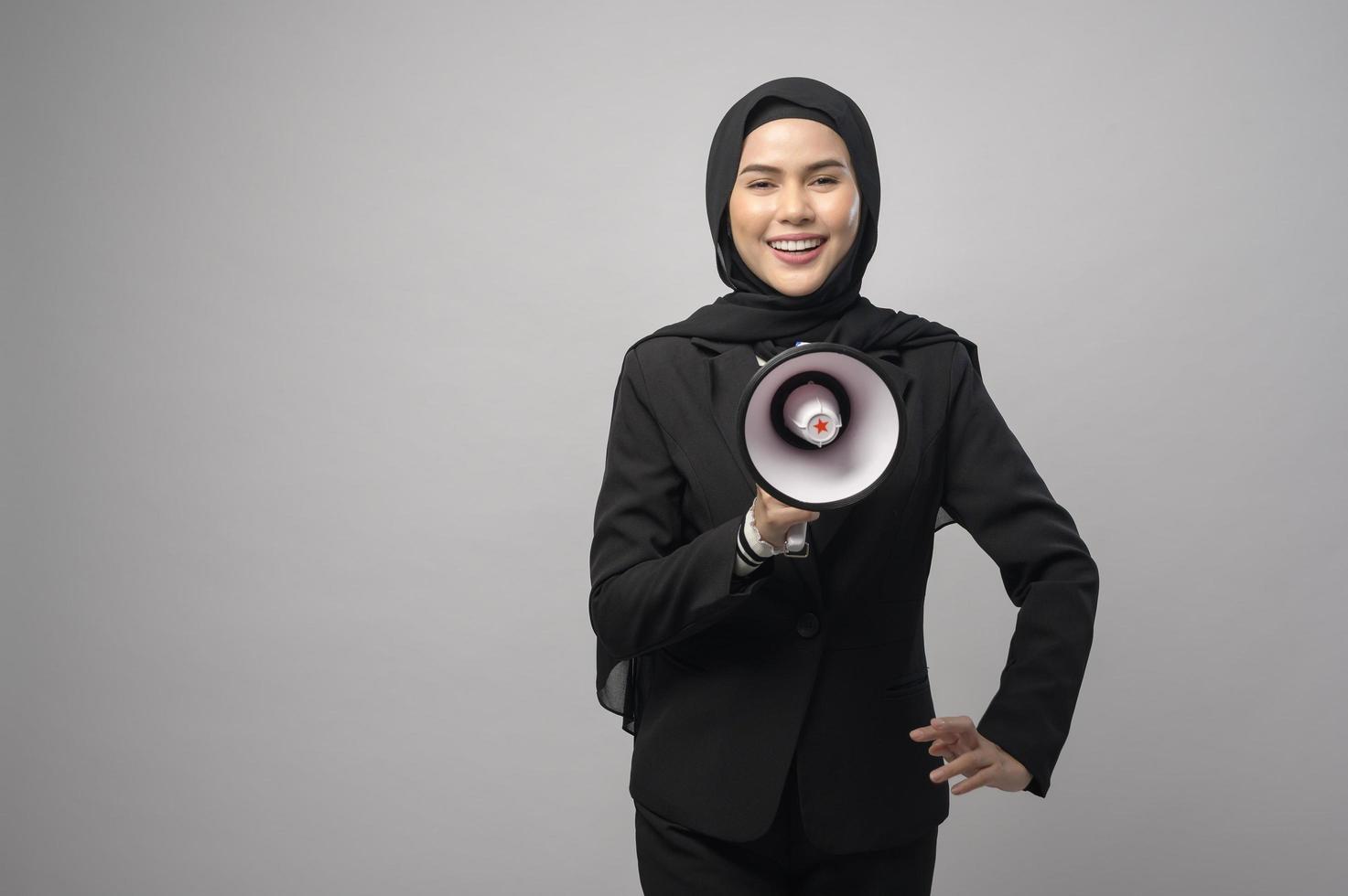 feliz mulher muçulmana está anunciando com megafone em fundo branco foto