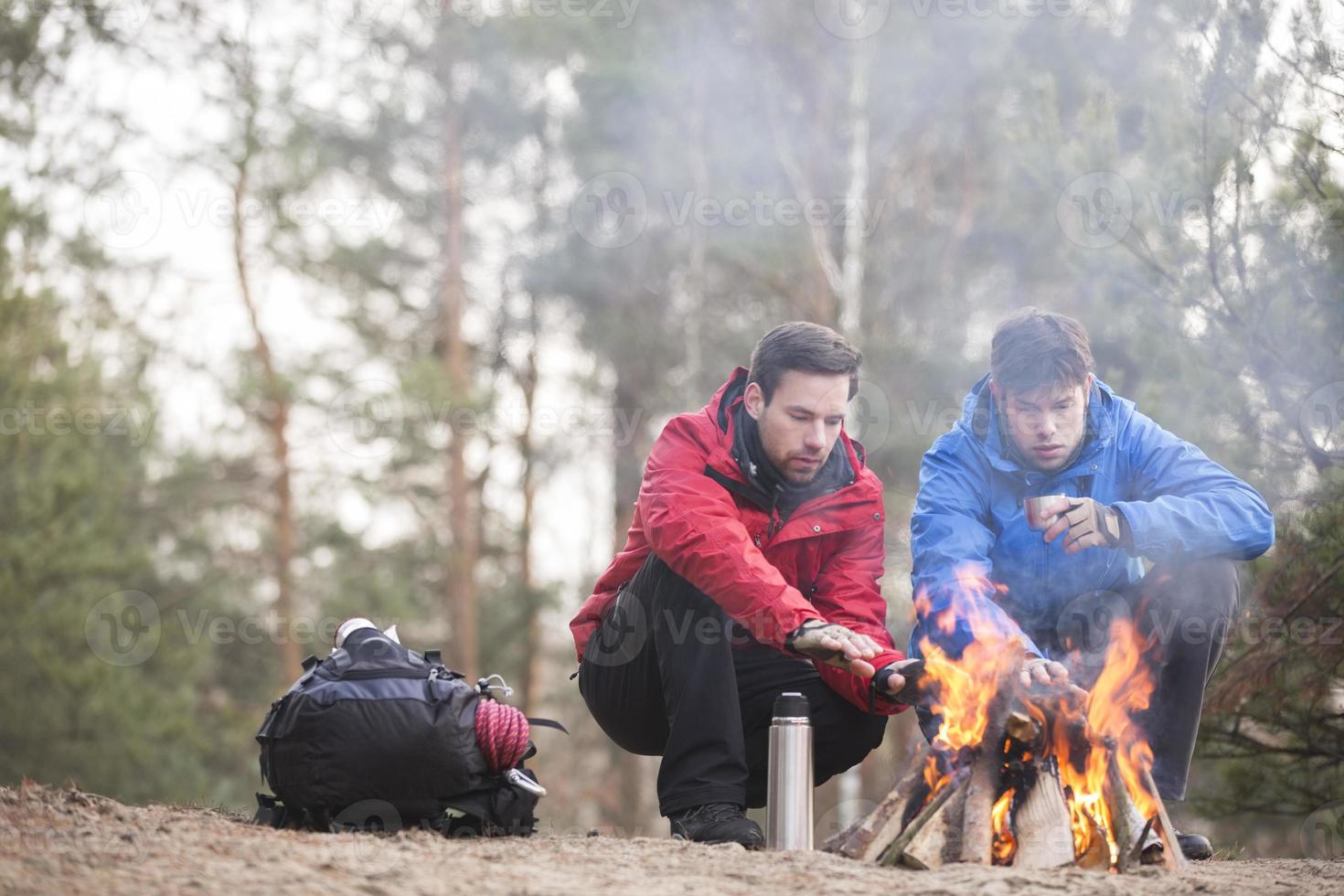 caminhantes masculinos aquecimento mãos na fogueira na floresta foto