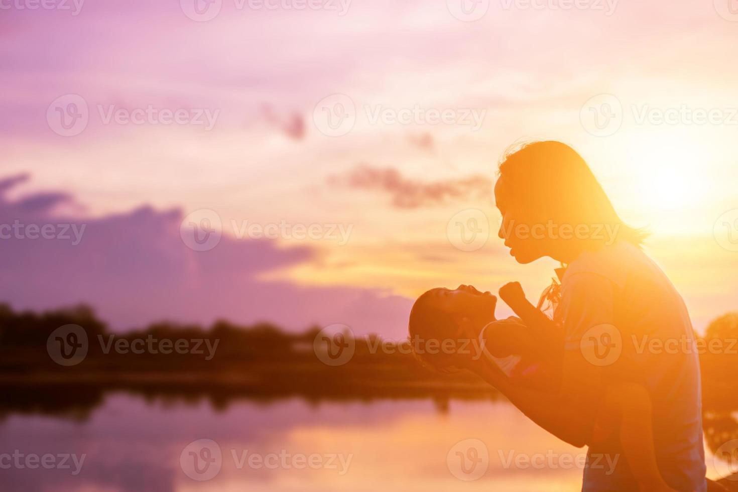 uma silhueta de uma criança feliz jovem os braços de sua mãe amorosa para um abraço, em frente ao pôr do sol no céu em um dia de verão. foto