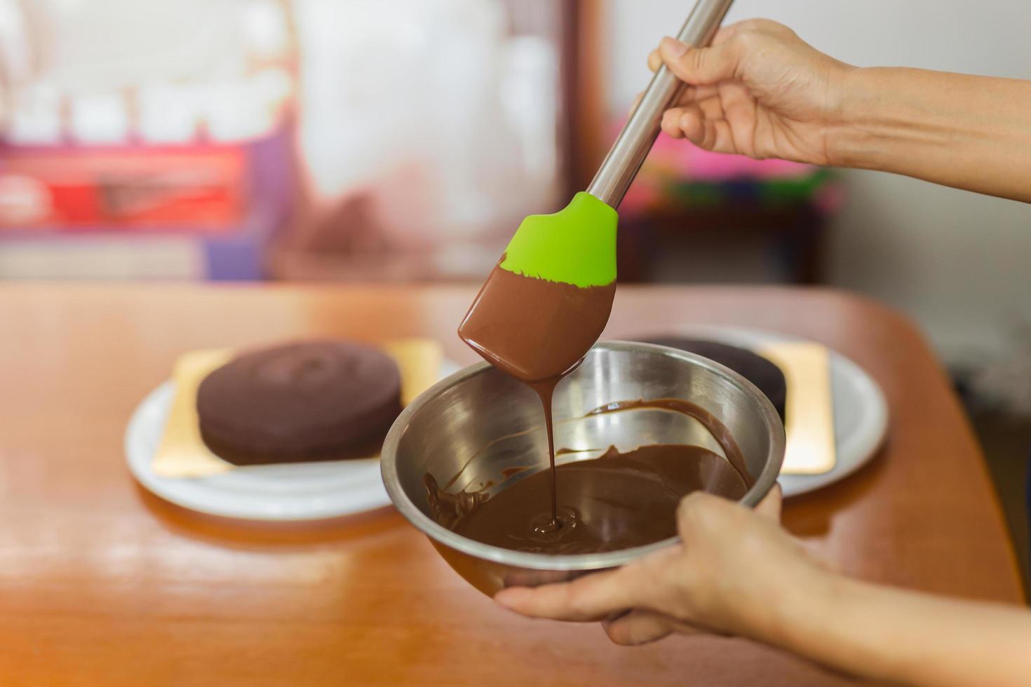 mulher misturando ganache de chocolate escuro delicioso suave com batedor na tigela de prata. foto