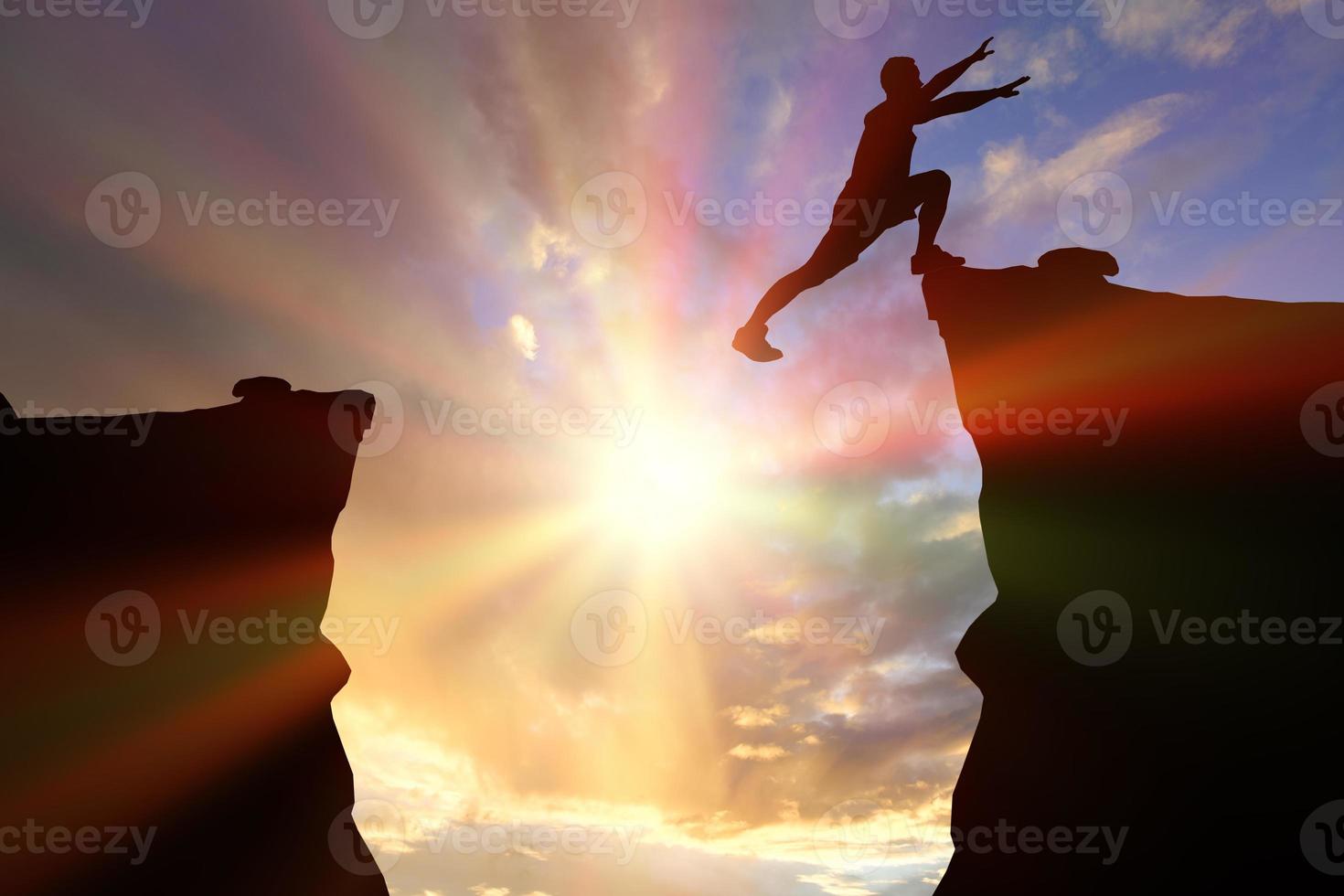 homem silhueta pulando sobre um precipício entre duas montanhas rochosas ao pôr do sol. liberdade, risco, desafio, conceito de sucesso. foto