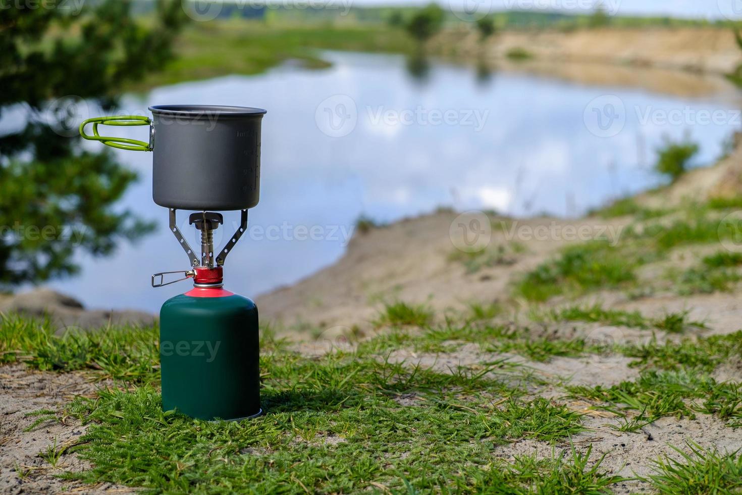 queimador turístico a gás com panela e rio de fundo foto