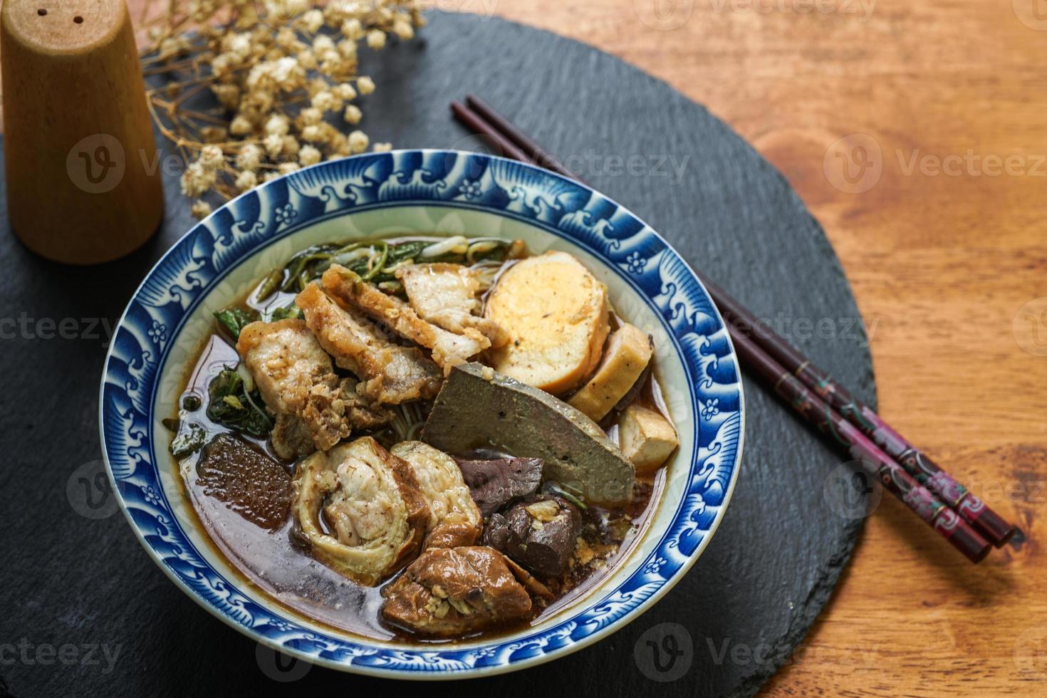 macarrão de arroz enrolado em caldo de cinco especiarias servido em um copo de azulejos em uma mesa de madeira. foto