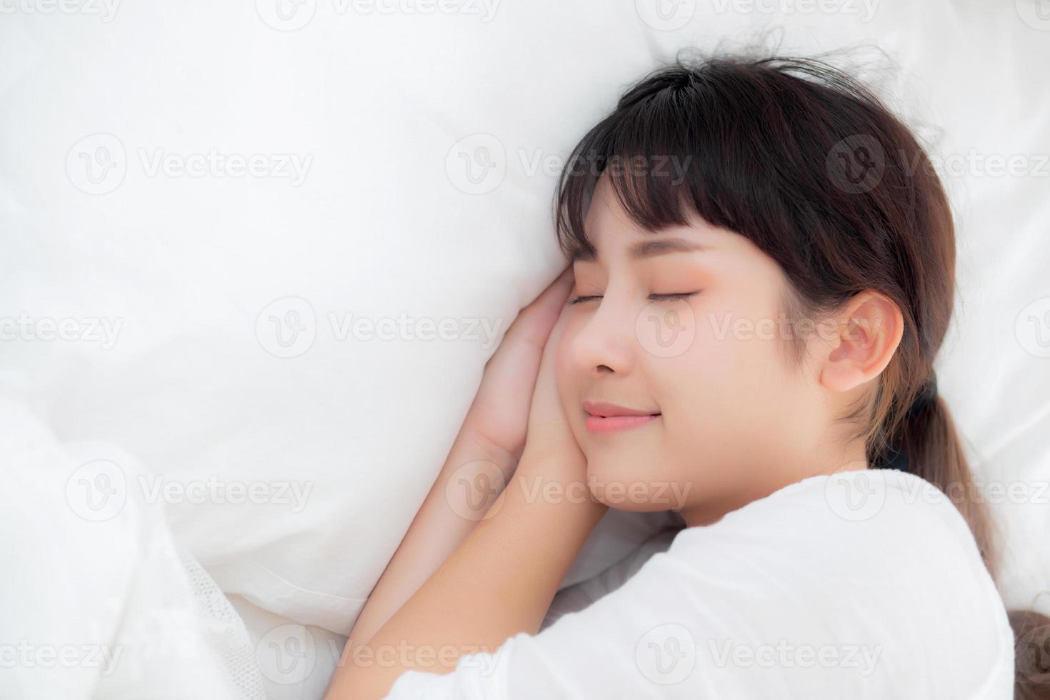 bela jovem asiática dormindo deitada na cama com a cabeça no travesseiro confortável e feliz. menina com relax para o conceito de saúde. foto