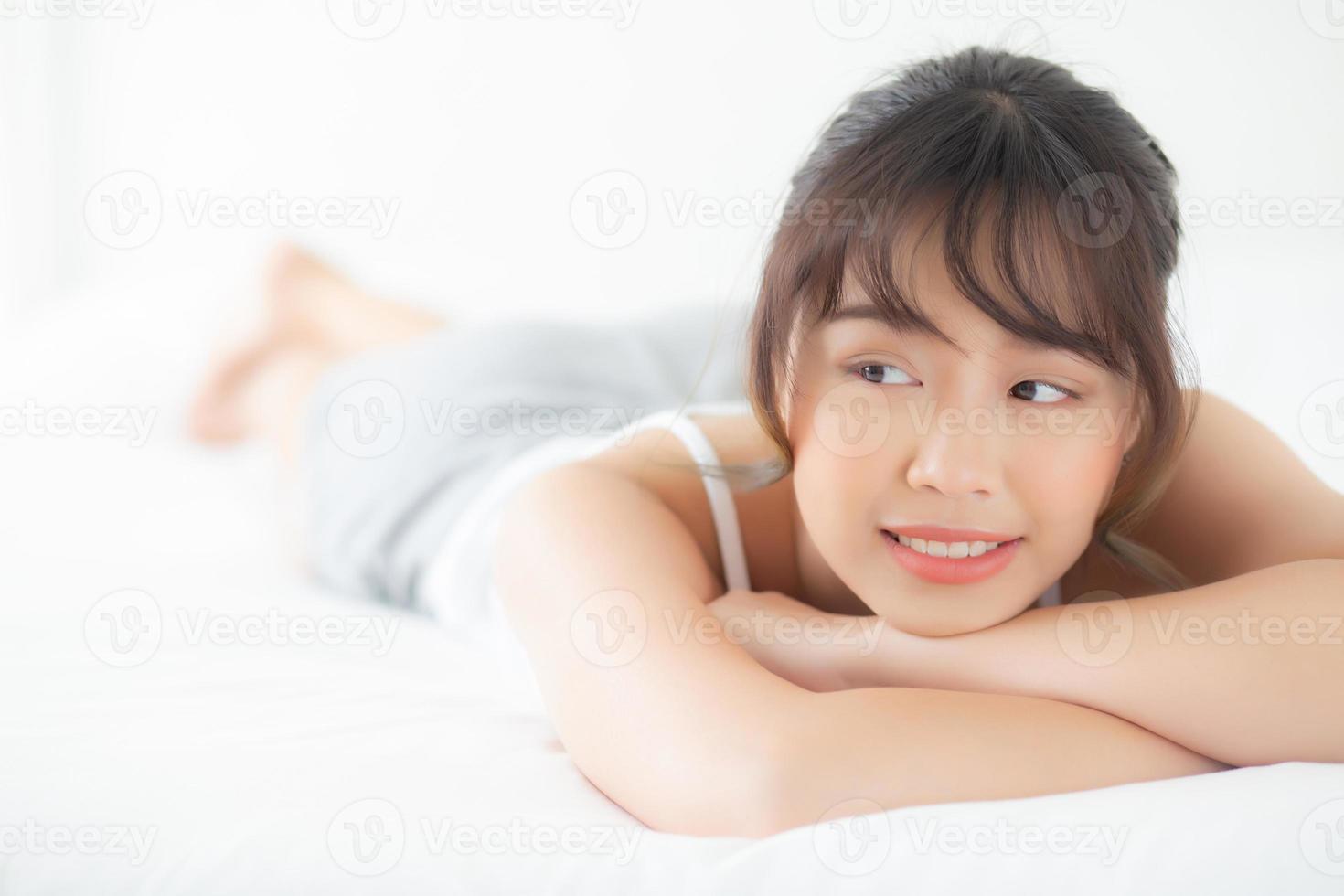 belo retrato jovem asiática deitada e sorrir enquanto acorda com o nascer do sol de manhã, beleza linda garota feliz e alegre descansando na cama no quarto, estilo de vida e conceito de relaxamento. foto