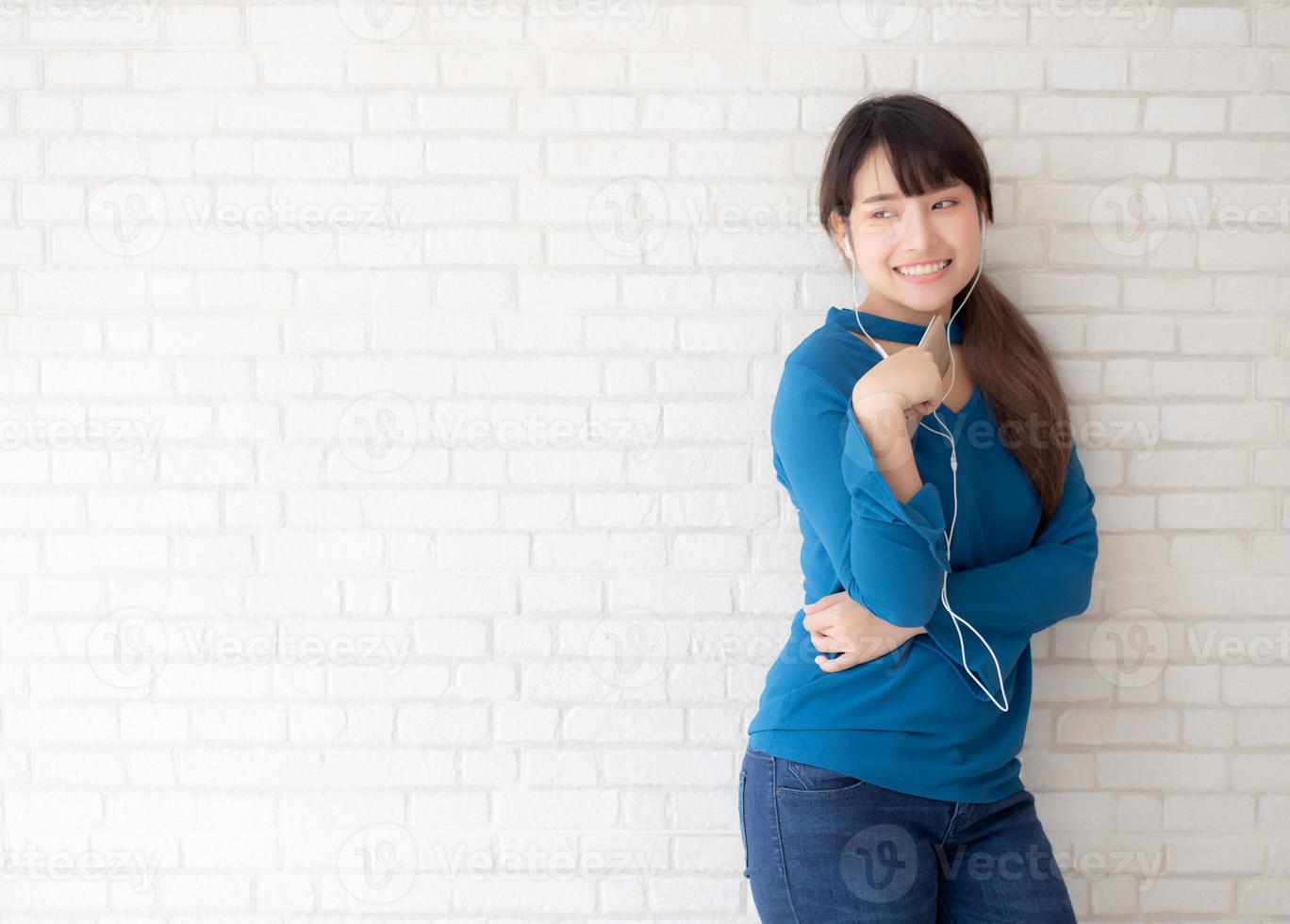 belo retrato asiático jovem em pé feliz desfrutar e diversão ouvir música com fone de ouvido no fundo de concreto de cimento, estilo de vida da menina relaxar rádio de som com fone de ouvido, conceito de tecnologia. foto