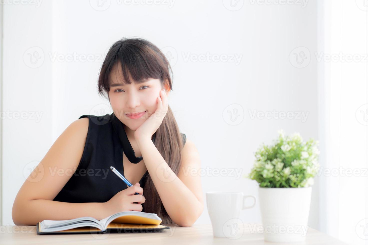 bela jovem asiática sorrindo sentado estudando e aprendendo a escrever caderno e diário na sala de estar em casa, lição de casa de menina, mulher de negócios trabalhando na mesa, conceito de educação. foto