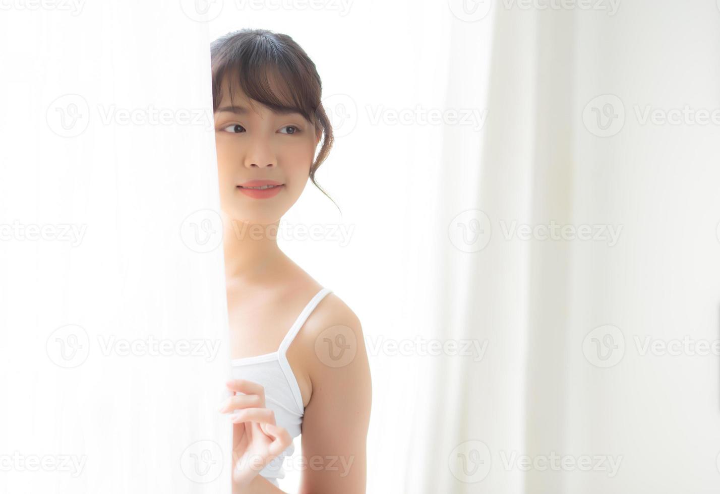 retrato de uma bela jovem asiática em pé na janela e sorria enquanto acorda com a luz do sol de manhã, garota feliz com fresco e alegre, estilo de vida e relaxe para o conceito de bem-estar. foto