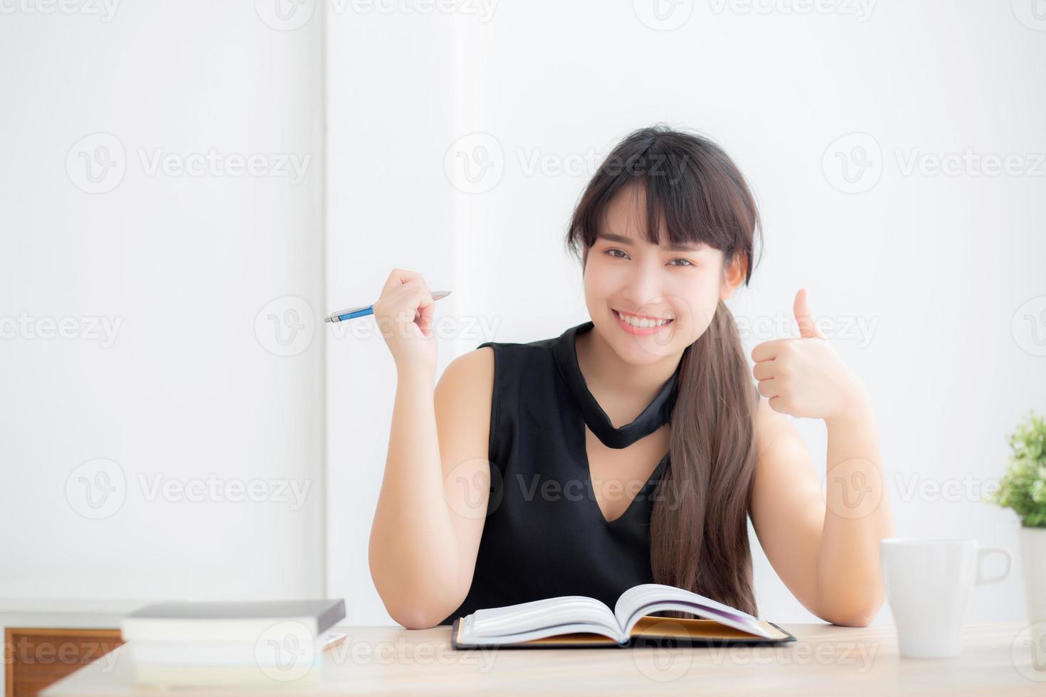 belo retrato jovem mulher asiática sorrindo sentado estudando e aprendendo a escrever caderno e diário na sala de estar em casa, lição de casa de menina, mulher de negócios trabalhando na mesa, conceito de educação. foto
