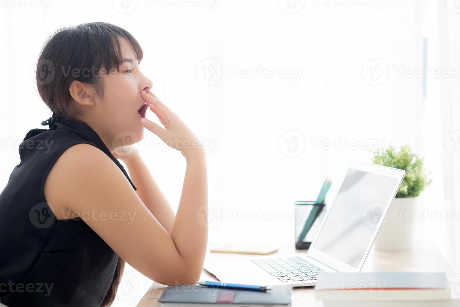 bela jovem mulher asiática freelance trabalhando entediado e cansado no computador portátil no escritório, menina preguiçosa com sono e bocejando no notebook, secretária feminina com exausto, conceito de negócio. foto