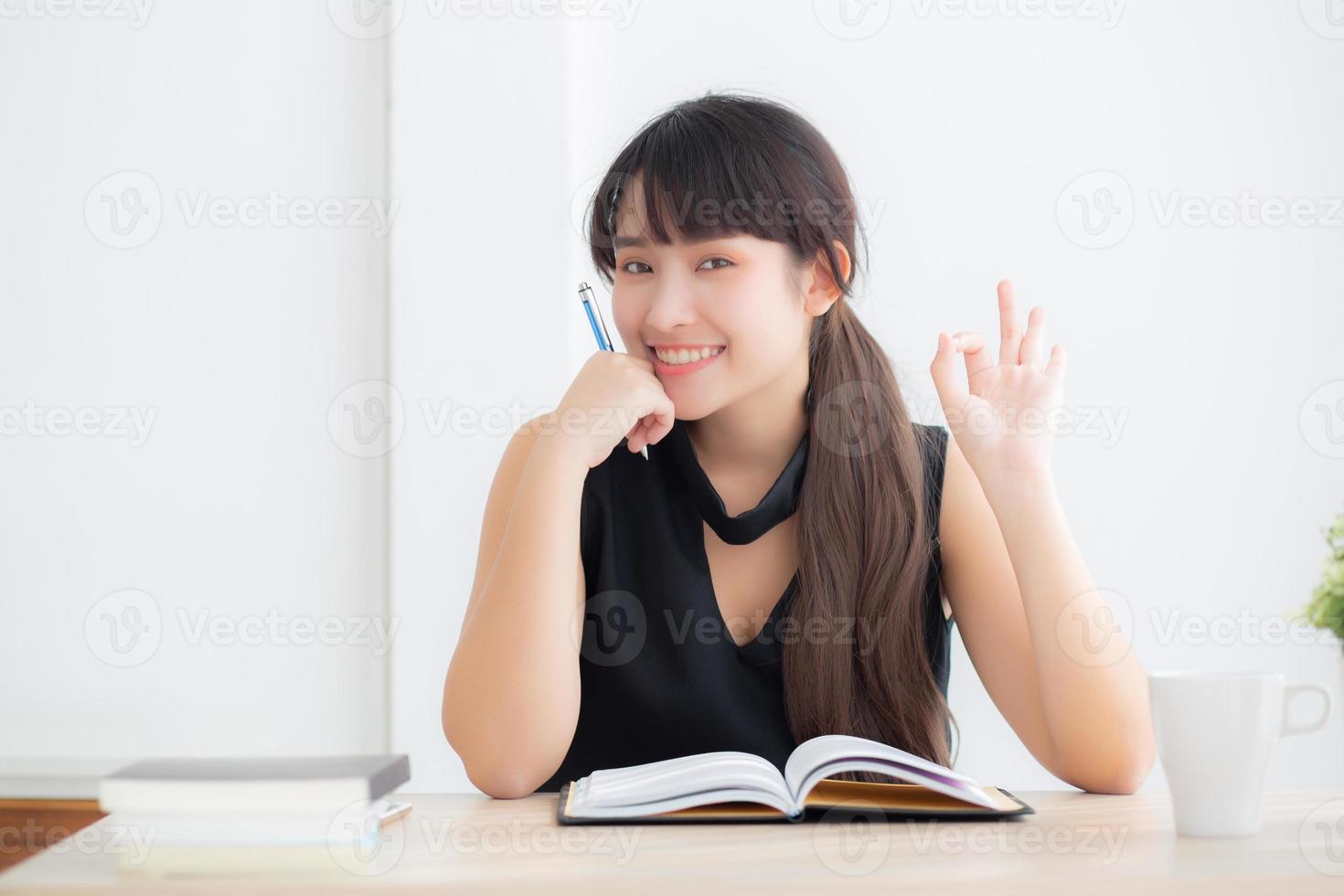 belo retrato jovem mulher asiática sorrindo sentado estudando e aprendendo a escrever caderno e diário na sala de estar em casa, lição de casa de menina, mulher de negócios trabalhando na mesa, conceito de educação. foto