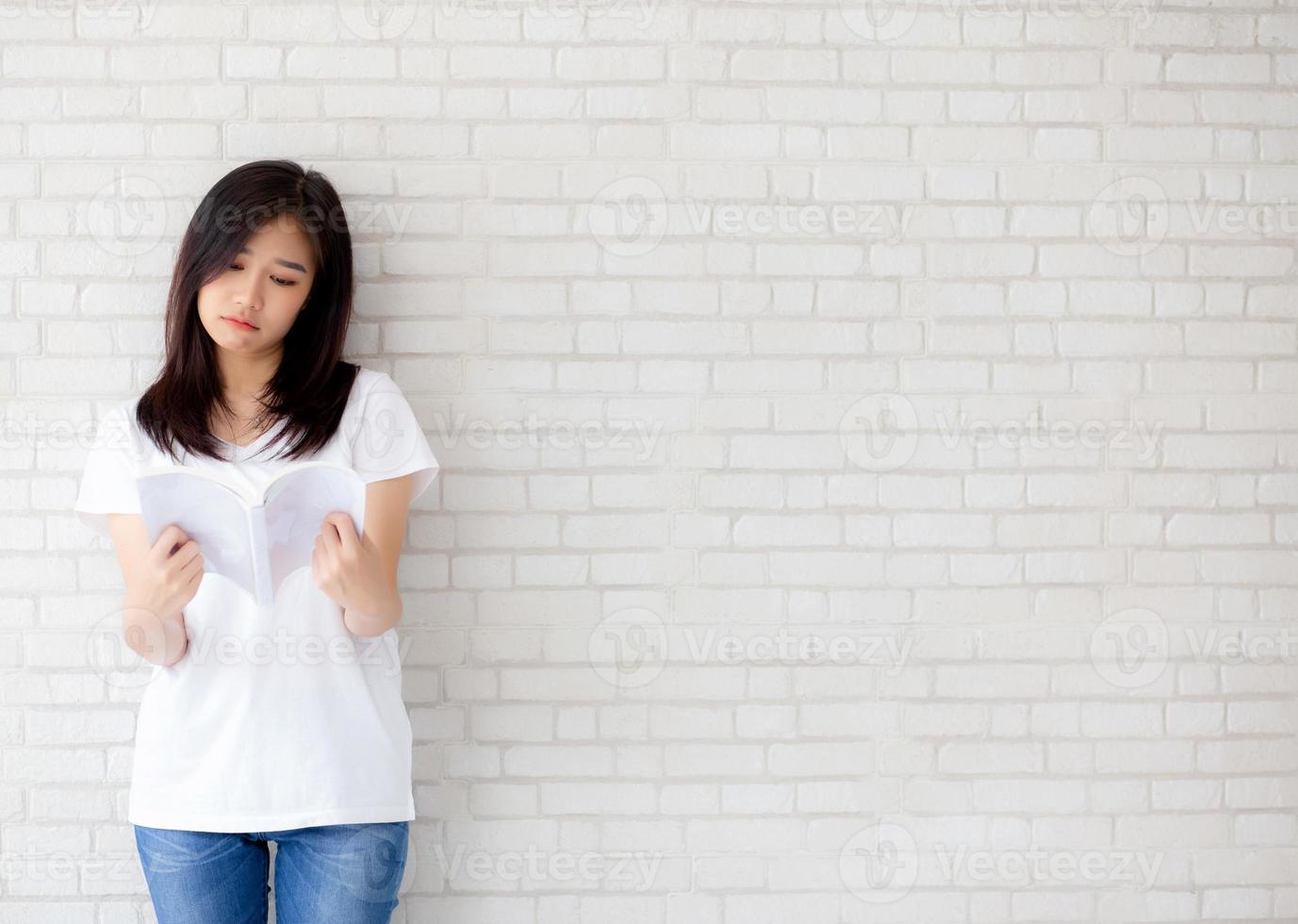 linda de retrato jovem mulher asiática felicidade relaxe em pé lendo livro sobre fundo branco de cimento concreto em casa, menina feliz estudo conteúdo literatura, educação e conceito de estilo de vida. foto