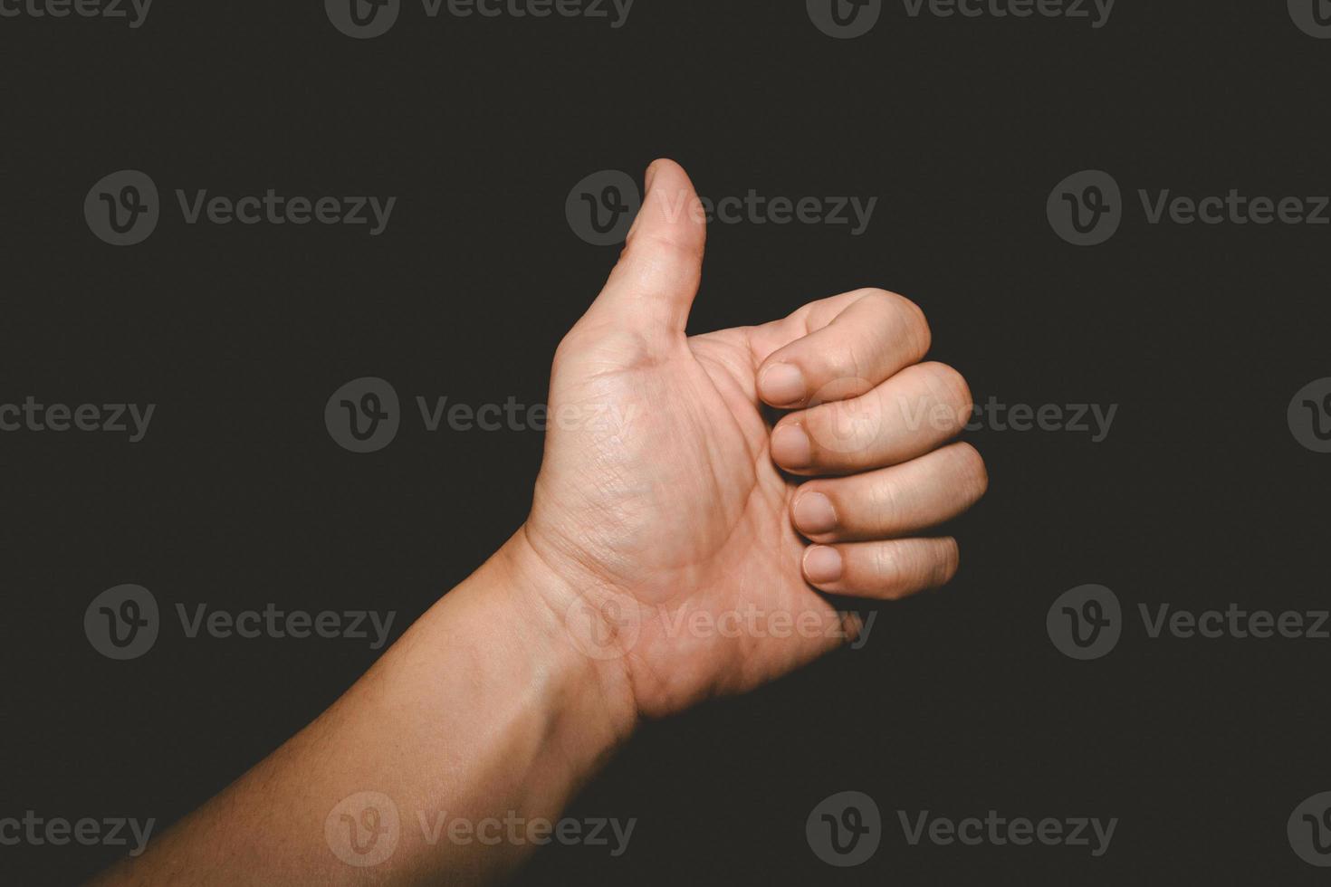 a mão do homem que polegares para cima é um símbolo de admiração em fundo preto foto