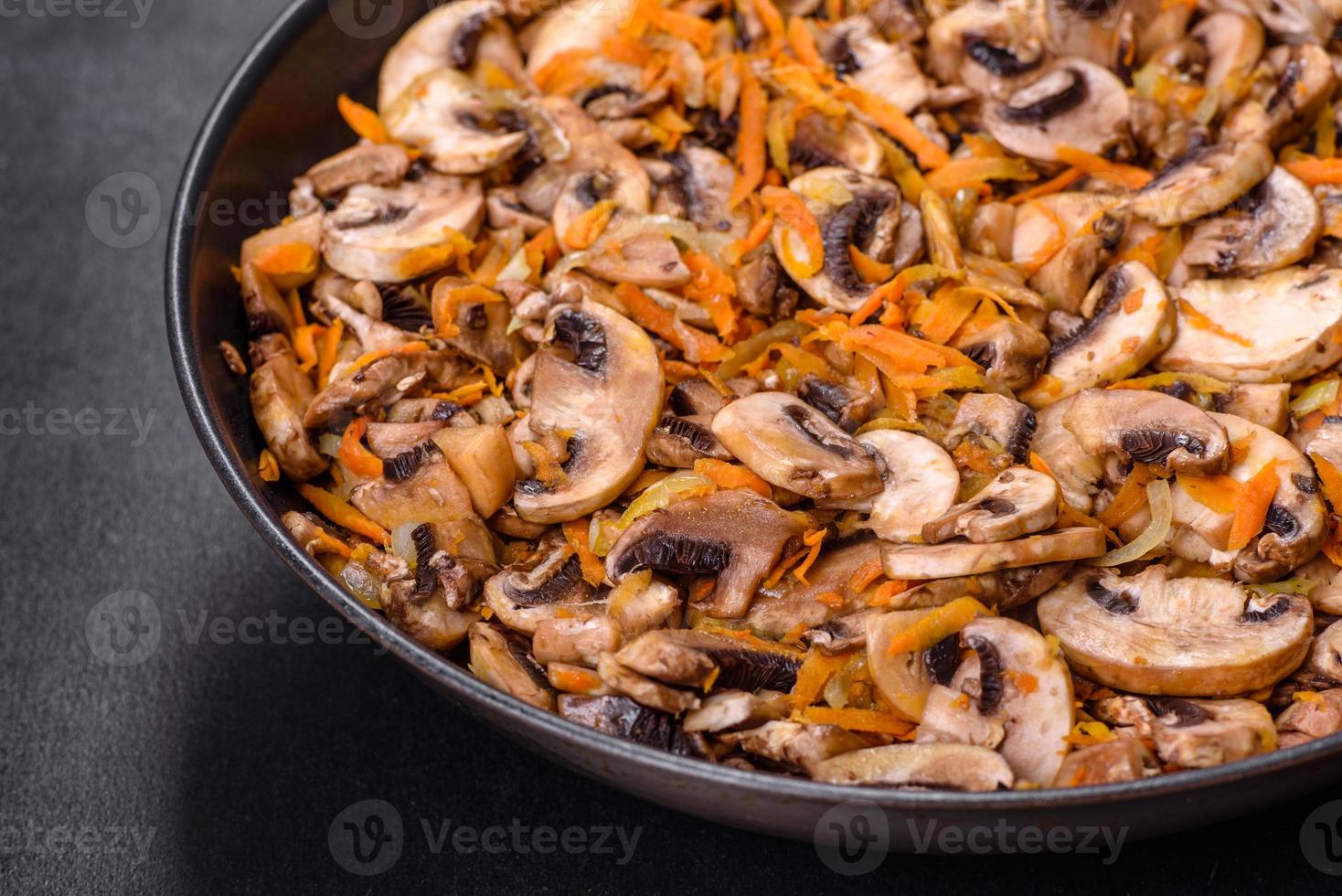 champignons fritos com cenoura, cebola e especiarias em uma panela contra um fundo escuro de concreto foto