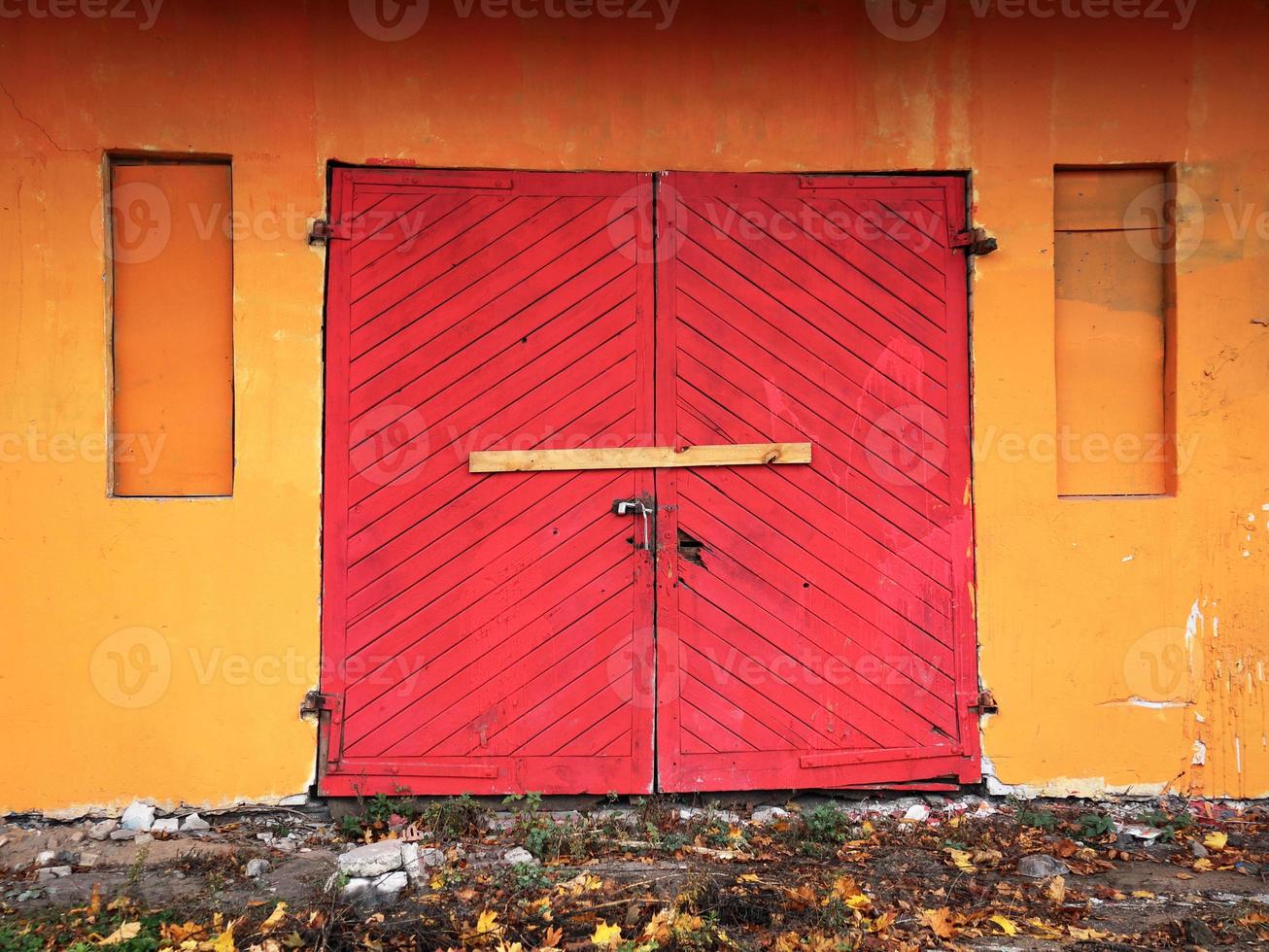 porta de entrada dupla de madeira velha vermelha brilhante porta de entrada no edifício de parede laranja trancada e pregada por uma prancha de madeira foto