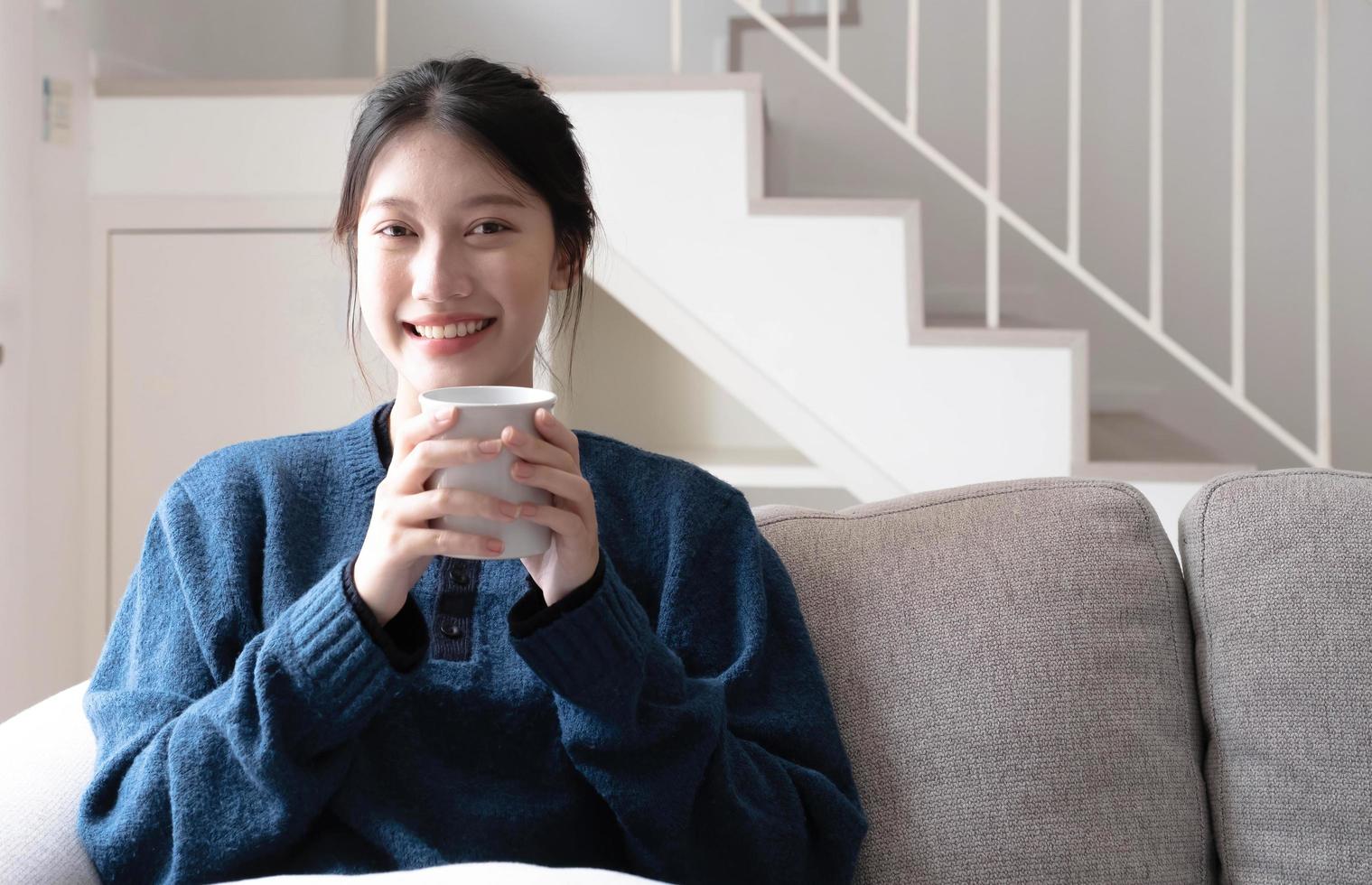 retrato de sorridente feliz alegre linda mulher asiática relaxante bebendo e olhando camara.girl felling desfrutar de tomar café da manhã nas férias de manhã de férias no sofá em casa foto