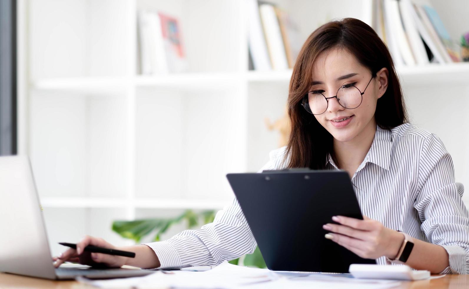 encantadora empresária asiática sentada trabalhando no laptop no escritório. foto