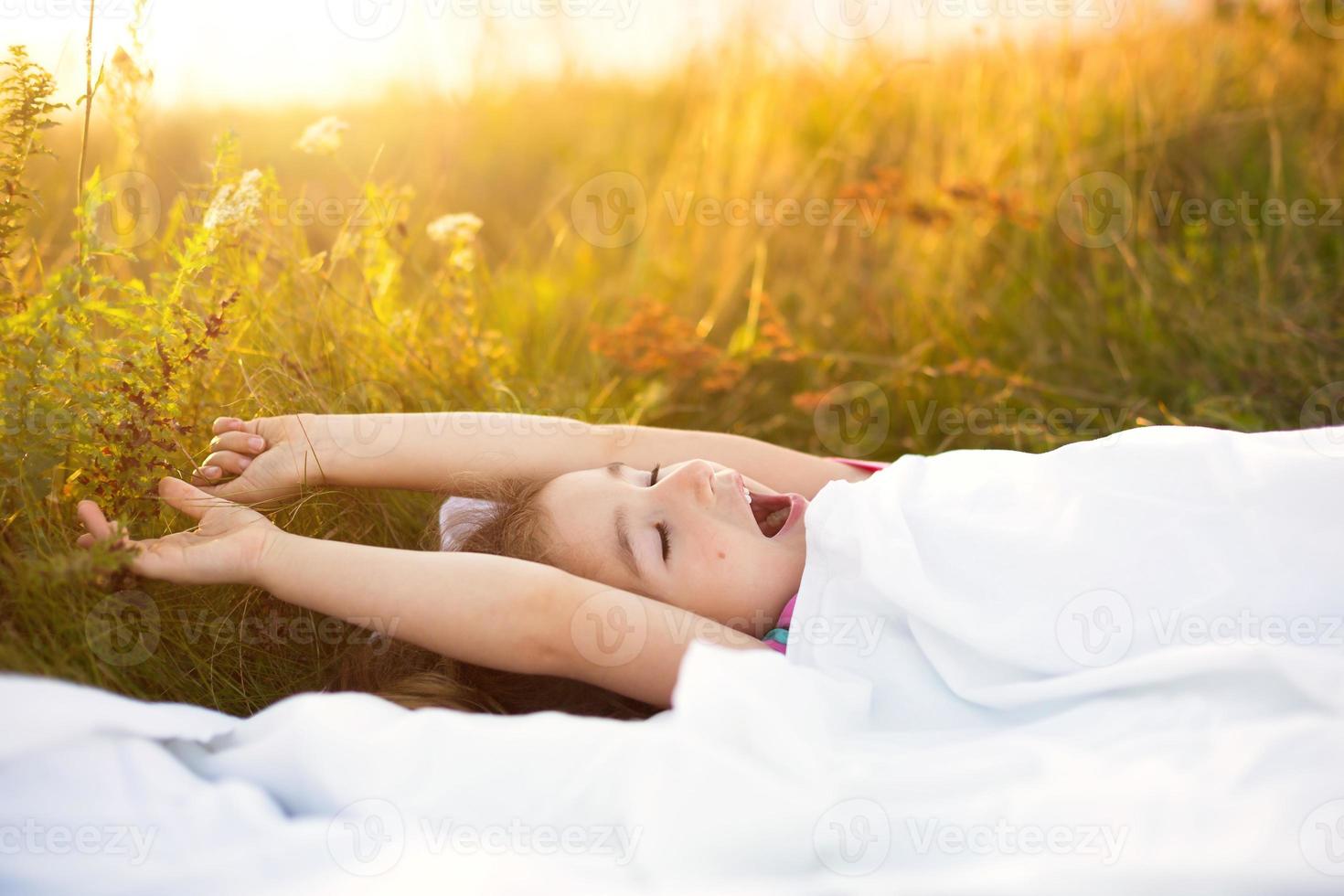 menina dorme na cama na grama, doce estica e boceja sonolenta, bom dia ao ar livre. ecologicamente correto, sono saudável, benefícios da ventilação, endurecimento, natureza limpa, ecologia, saúde infantil foto