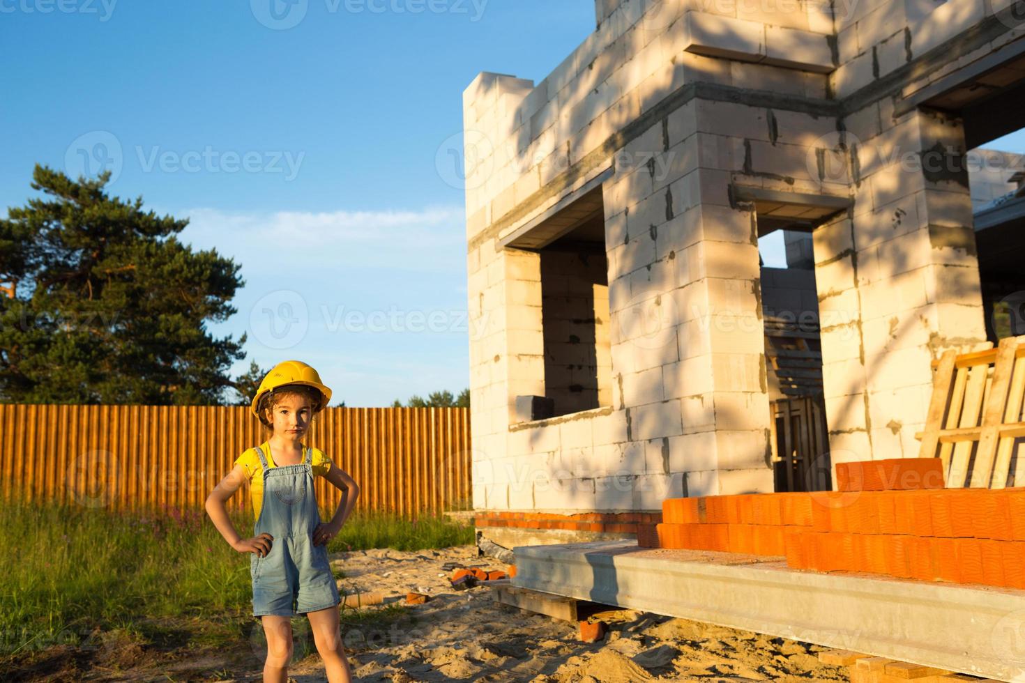 uma garotinha de capacete amarelo está brincando de construtor no canteiro de obras de sua futura casa. sonhos de se mudar, escolher uma profissão, educação dos filhos. foto