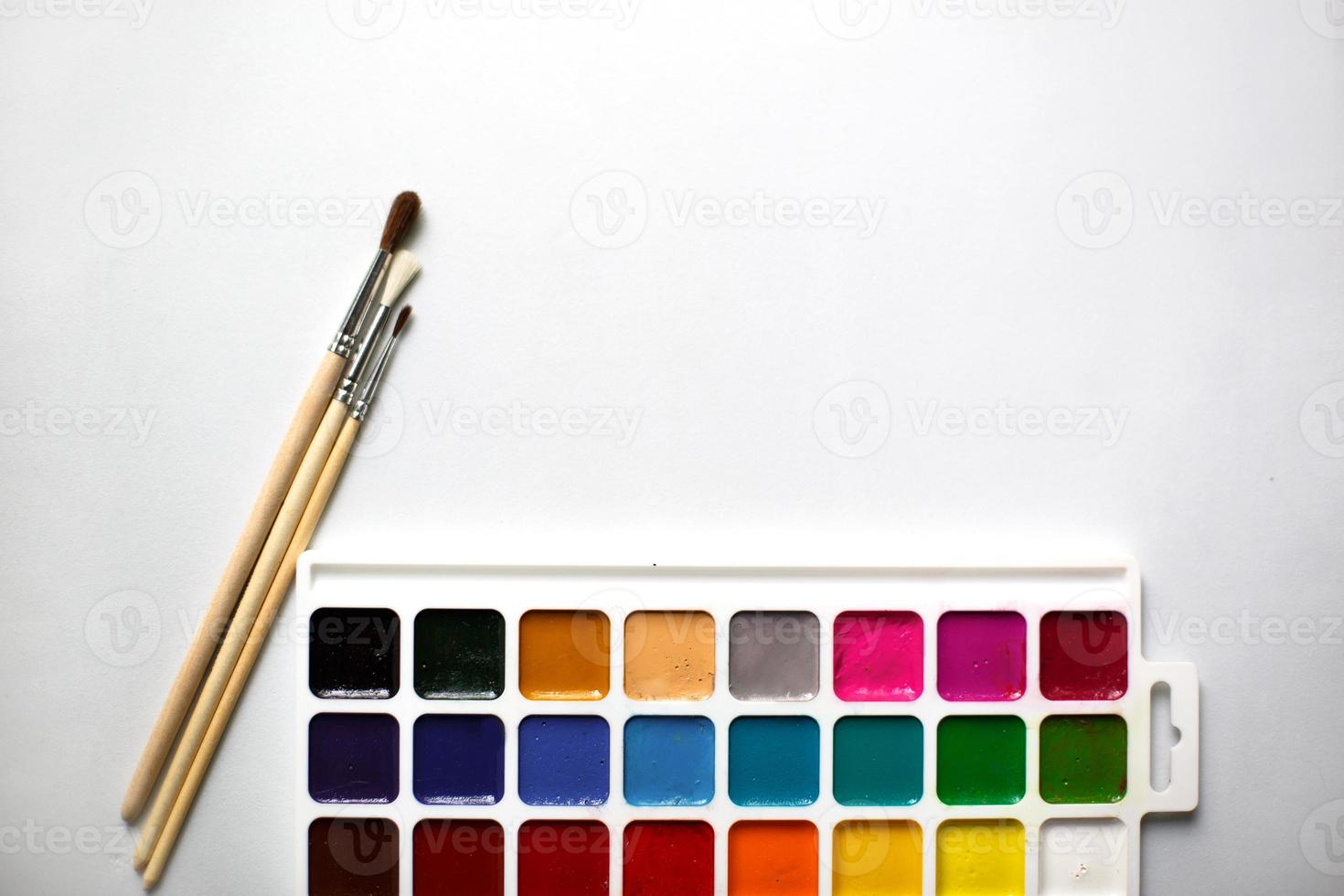 uma paleta de aquarelas de dezoito cores e pincéis em um fundo branco com espaço para texto. foto