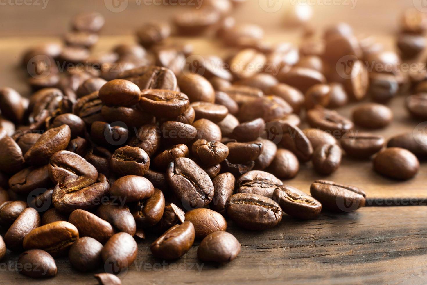 grãos de café torrados perto - fundo perfumado. grãos de café arábica marrom estão espalhados na mesa de madeira. espaço de cópia foto
