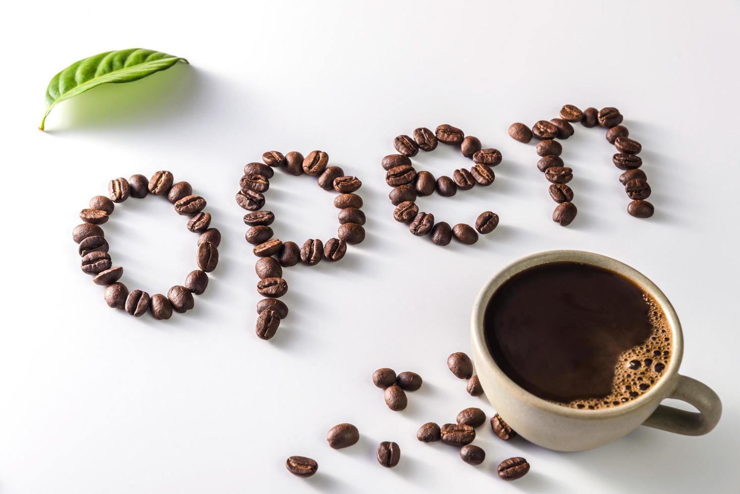 xícara de café e grãos de café em fundo branco com texto aberto feito de grãos de café foto
