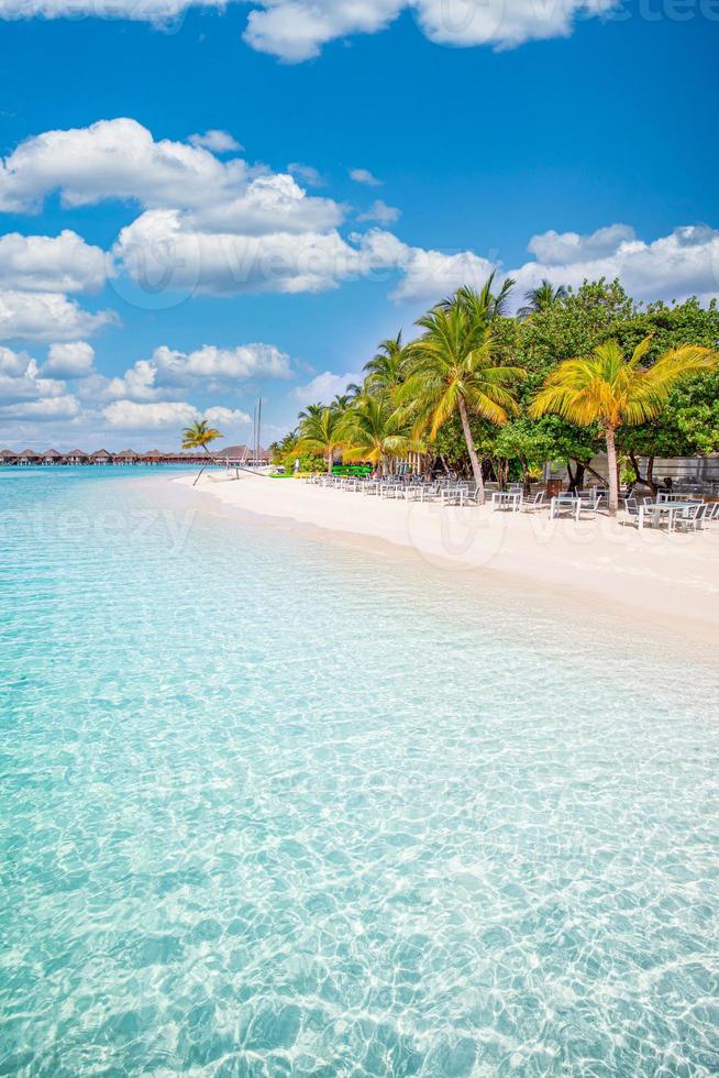 resort de praia paradisíaco com palmeiras e guarda-sóis de palha e mar tropical na ilha das maldivas. férias de verão e conceito de praia tropical. foto