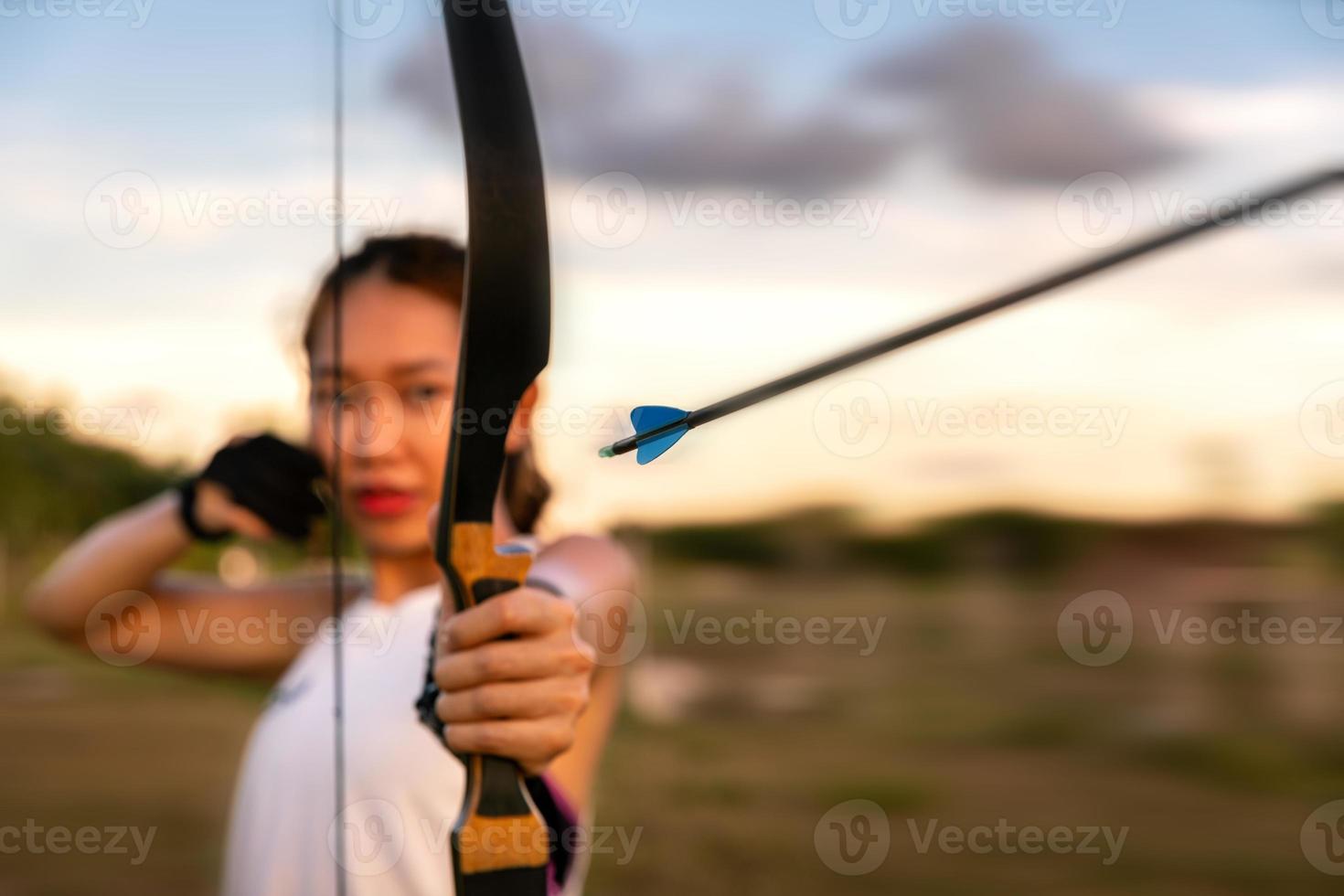 jovem arqueira feminina, tiro com arco, atirar arow com arco no campo da natureza para o alvo, conceito de sucesso, no campo para exercício esportivo na hora do pôr do sol foto