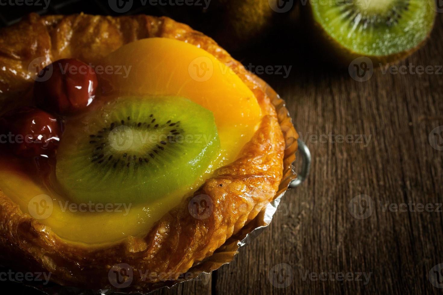 torta de frutas com kiwi, cereja, caqui, colocada em tira de aço no banco de madeira com fundo preto, close-up foto