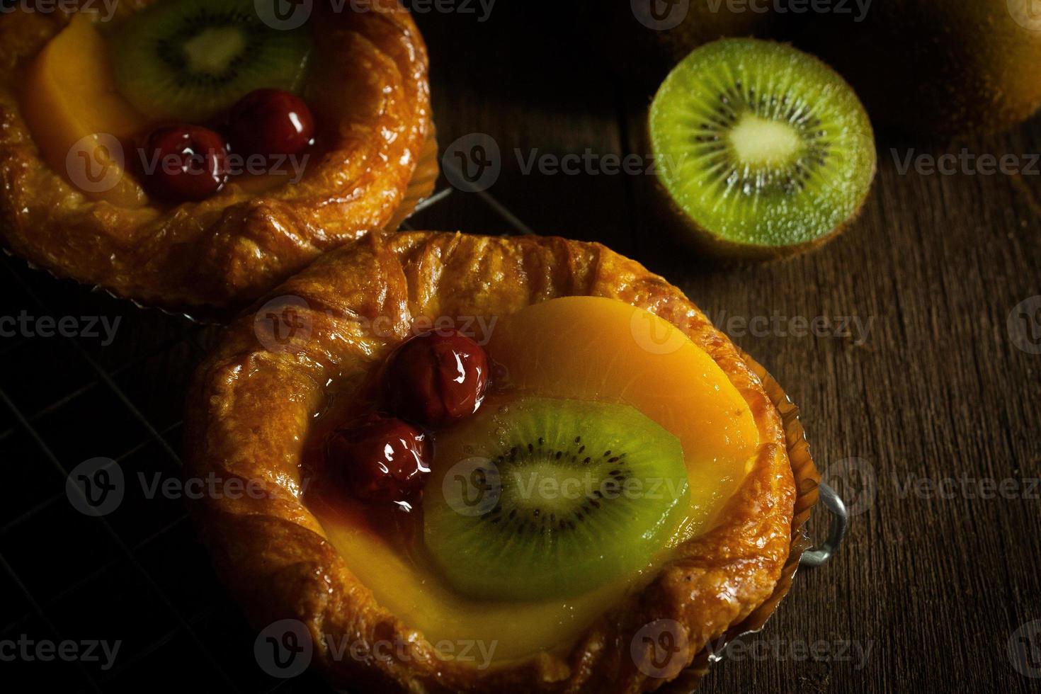 torta de frutas com kiwi, cereja, caqui, coloque em tira de aço no banco de madeira com fundo preto foto