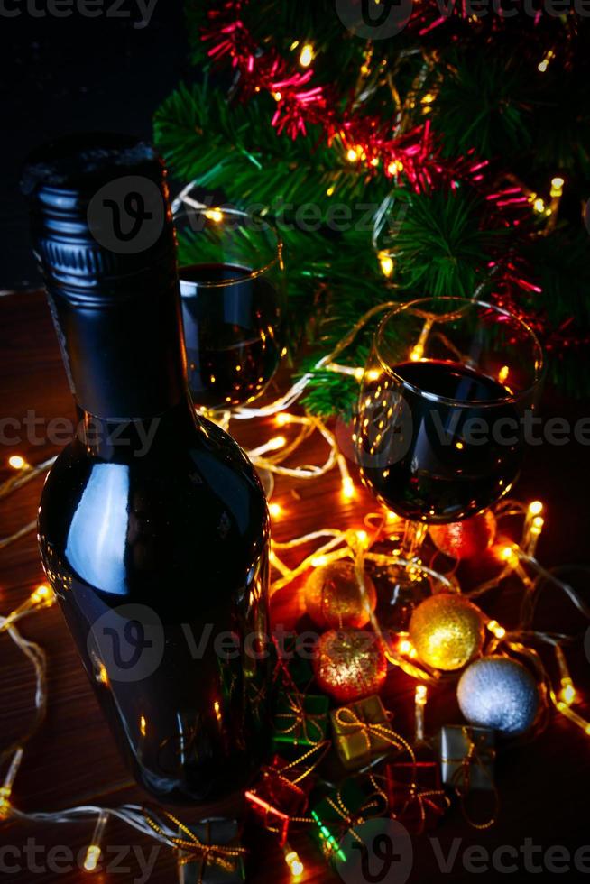 vinho tinto em vidro transparente, árvore de natal e enfeite na mesa de madeira pronta para comemorar. foto