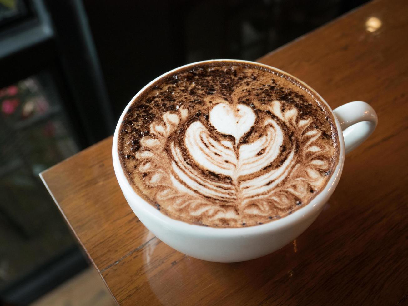 cappuccino com espuma de leite fresco e latte art em um vidro cerâmico branco em uma mesa de madeira em um café. foto