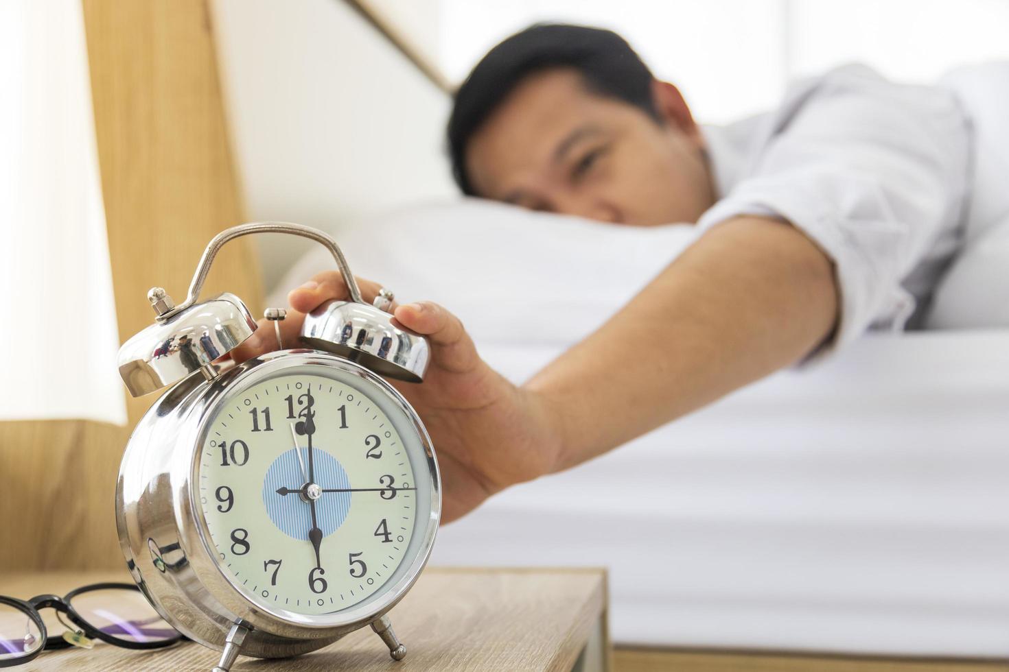 homem preguiçosamente reahting sua mão para desligar o despertador às 6 da manhã. depois de acordar de manhã na cama aconchegante com foto