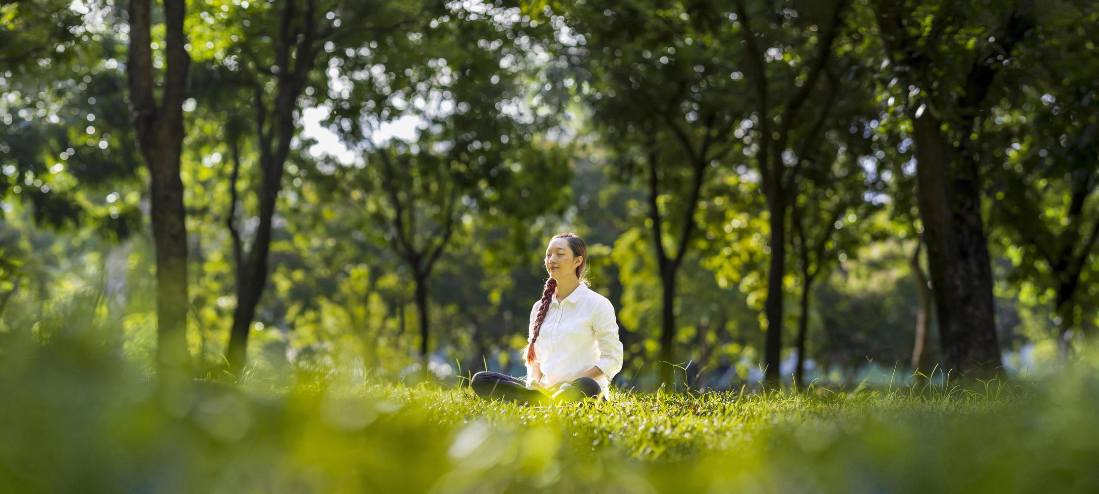 mulher praticando relaxantemente meditação na floresta para alcançar a felicidade da sabedoria da paz interior com feixe de luz do sol para o conceito de mente e alma saudável foto