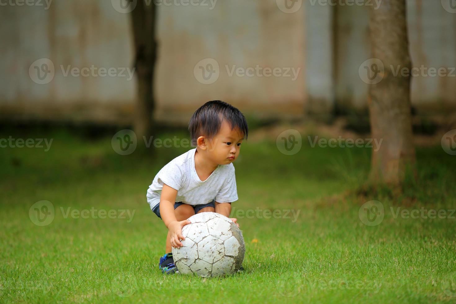 menino asiático jogando futebol no parque. garoto com bola no campo de grama. foto