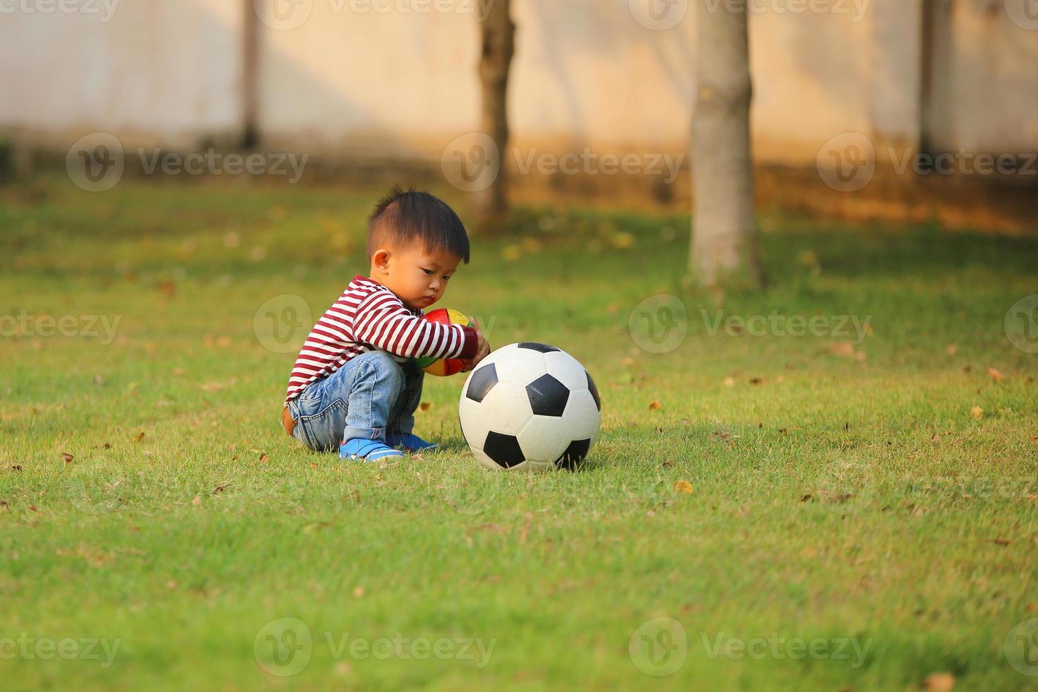 menino asiático jogando futebol no parque. garoto com bolas no campo de grama. foto