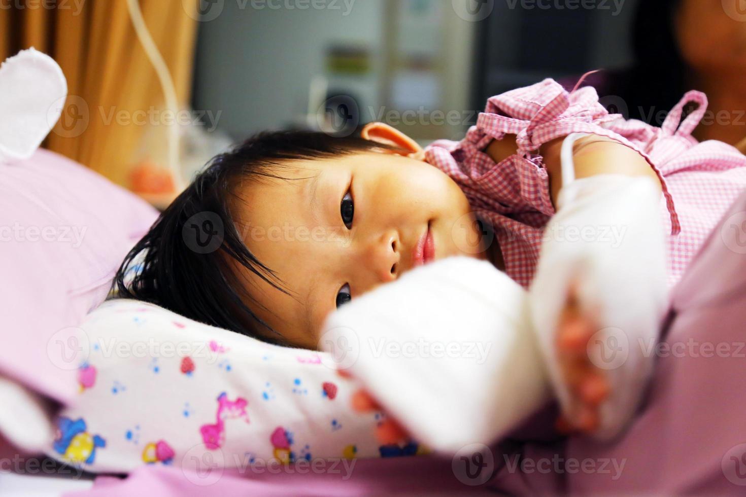 bebê asiático está com febre, em seguida, admitido no hospital e tem tubo iv com almofada nas mãos para proteger a agulha do medicamento. foto