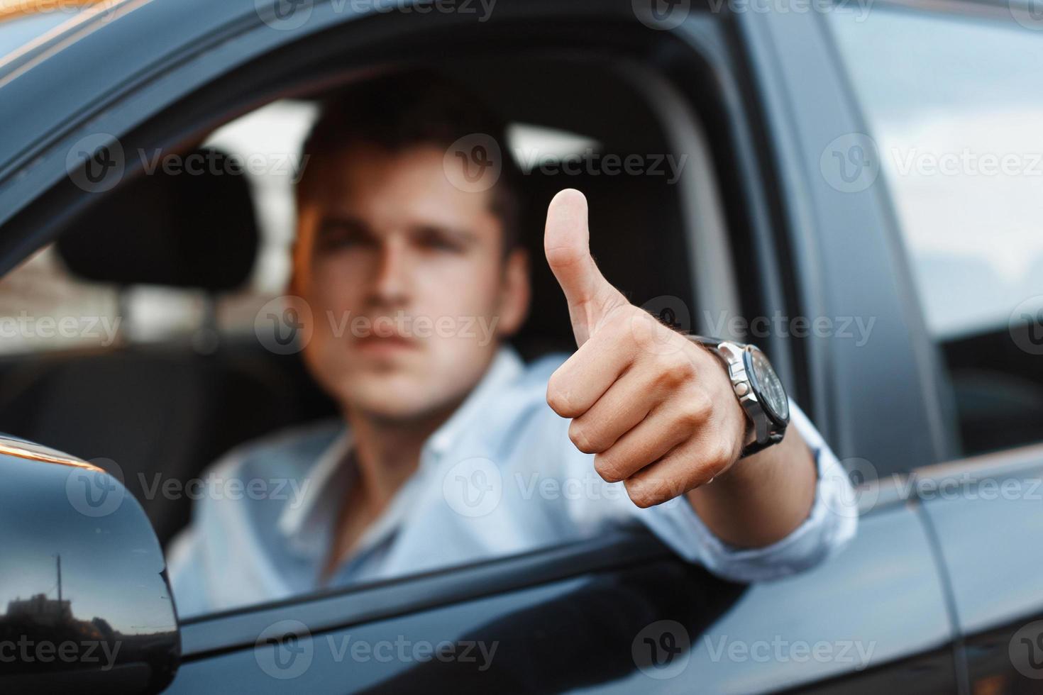 homem bonito, sentado em um carro e segurando os polegares foto