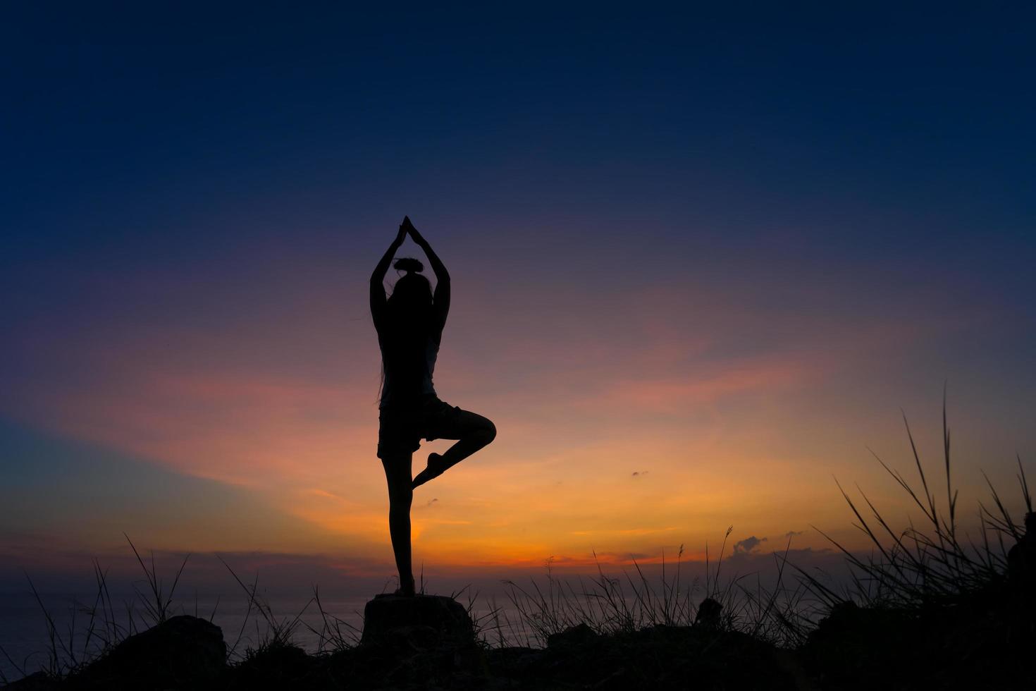 silhueta de mulher praticando guerreiro uma pose de ioga na praia ao pôr do sol foto