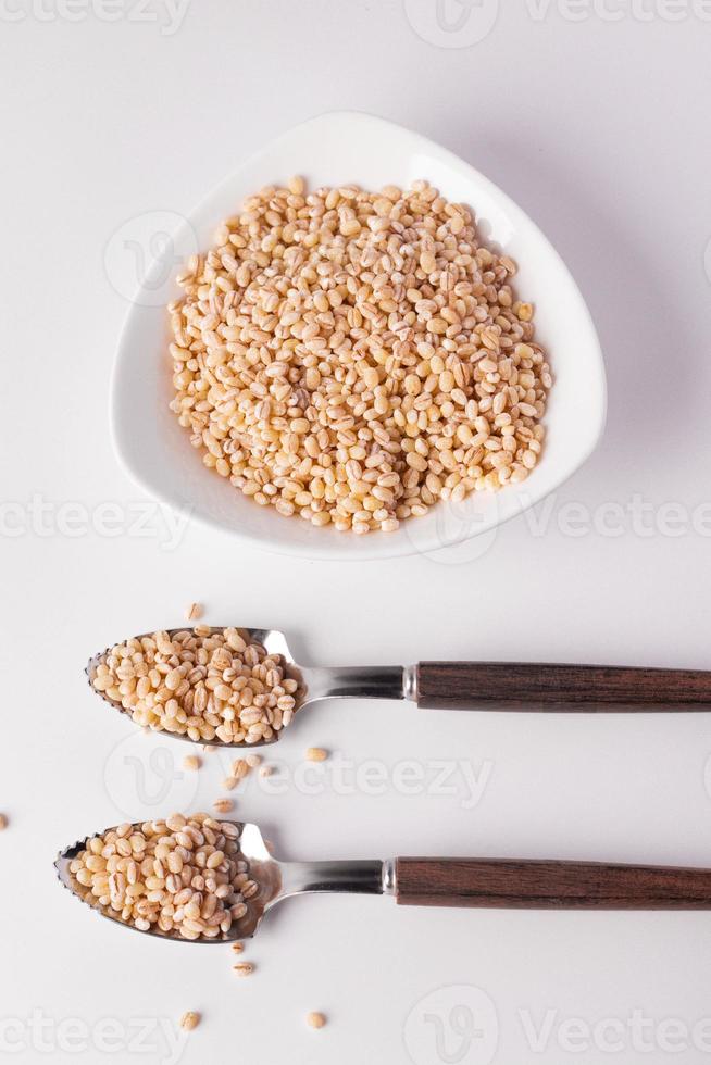 arroz de cevada no copo de cerâmica e colher no fundo branco foto