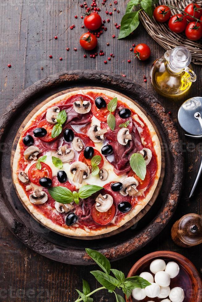 pizza italiana com salame, cogumelos e azeitonas na mesa de madeira foto