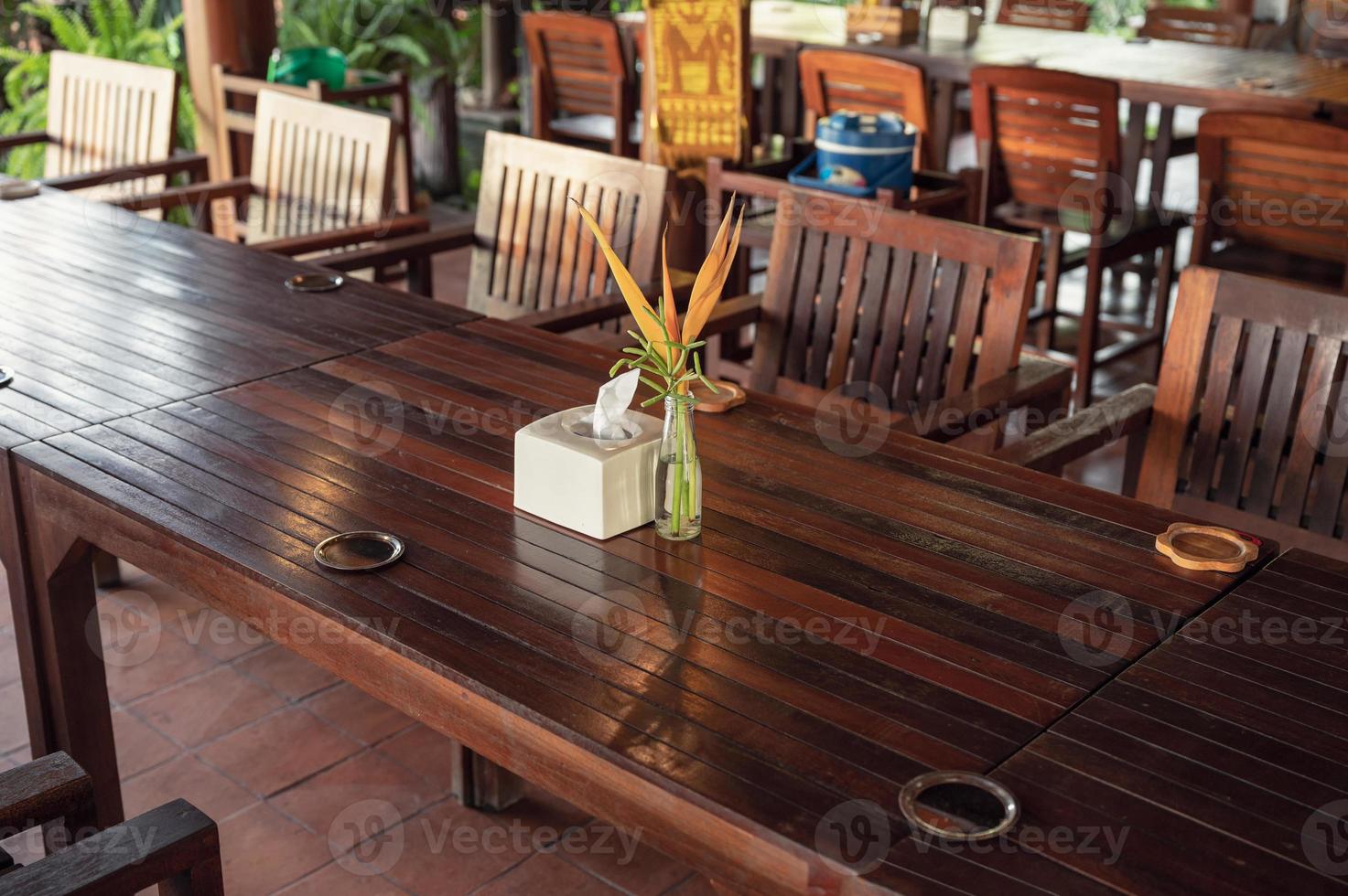 preparação de mesa de jantar de madeira e cadeiras com flor em vaso e guardanapo no restaurante foto