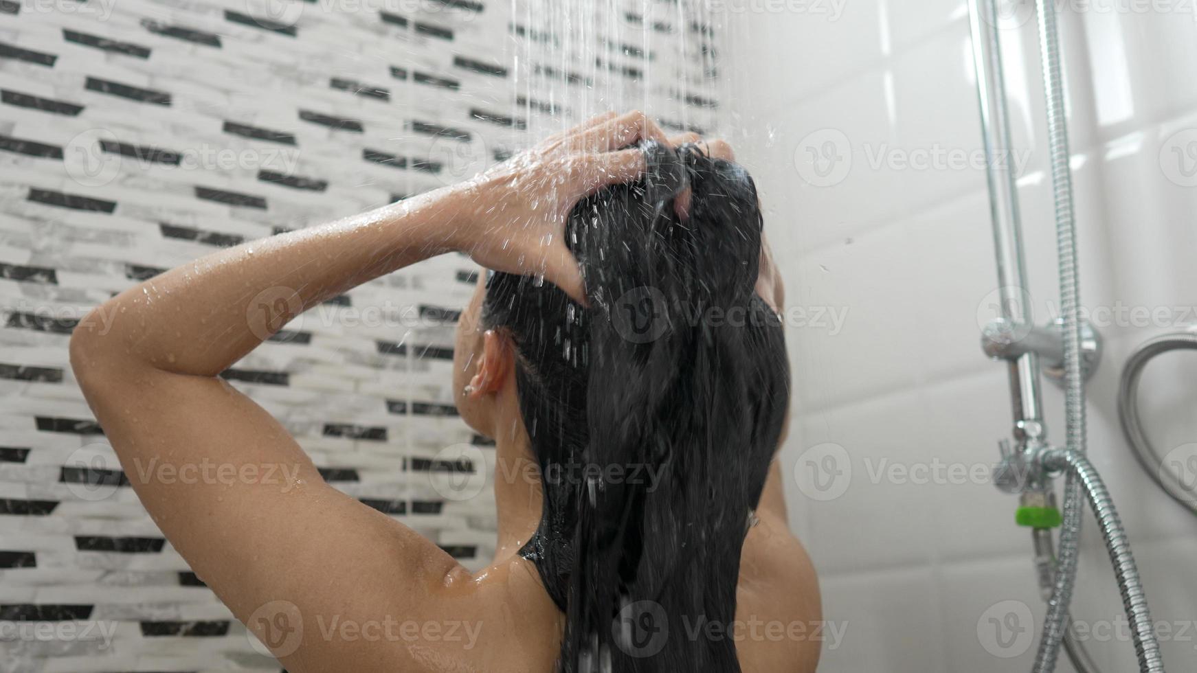 jovem tomando banho e lavando o cabelo no banheiro foto