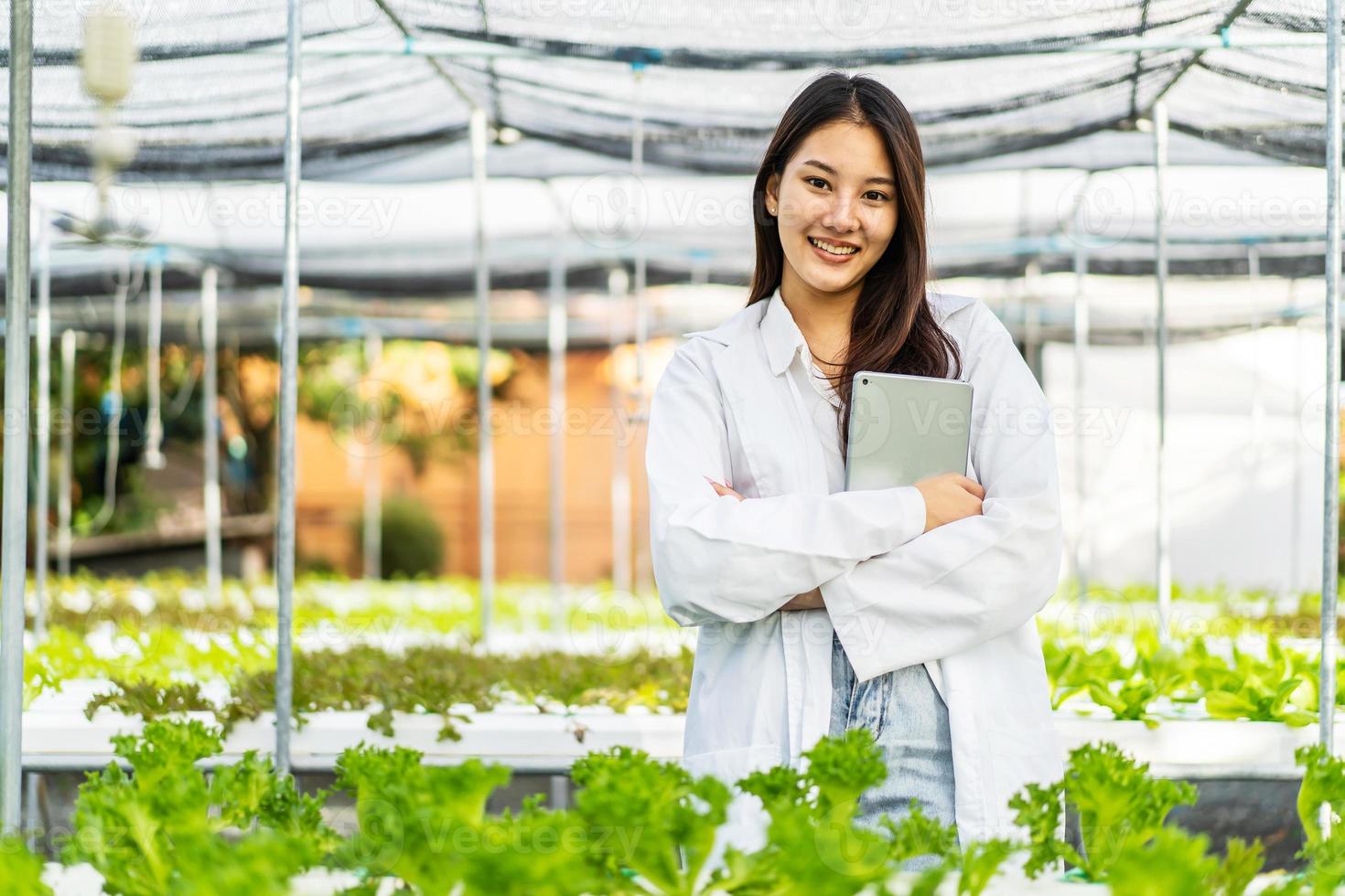 mulher pesquisadora de fazenda asiática em pé com os braços cruzados cuida dos vegetais que crescem na fazenda. a agricultura é a agricultura sustentável para os alimentos do futuro. foto
