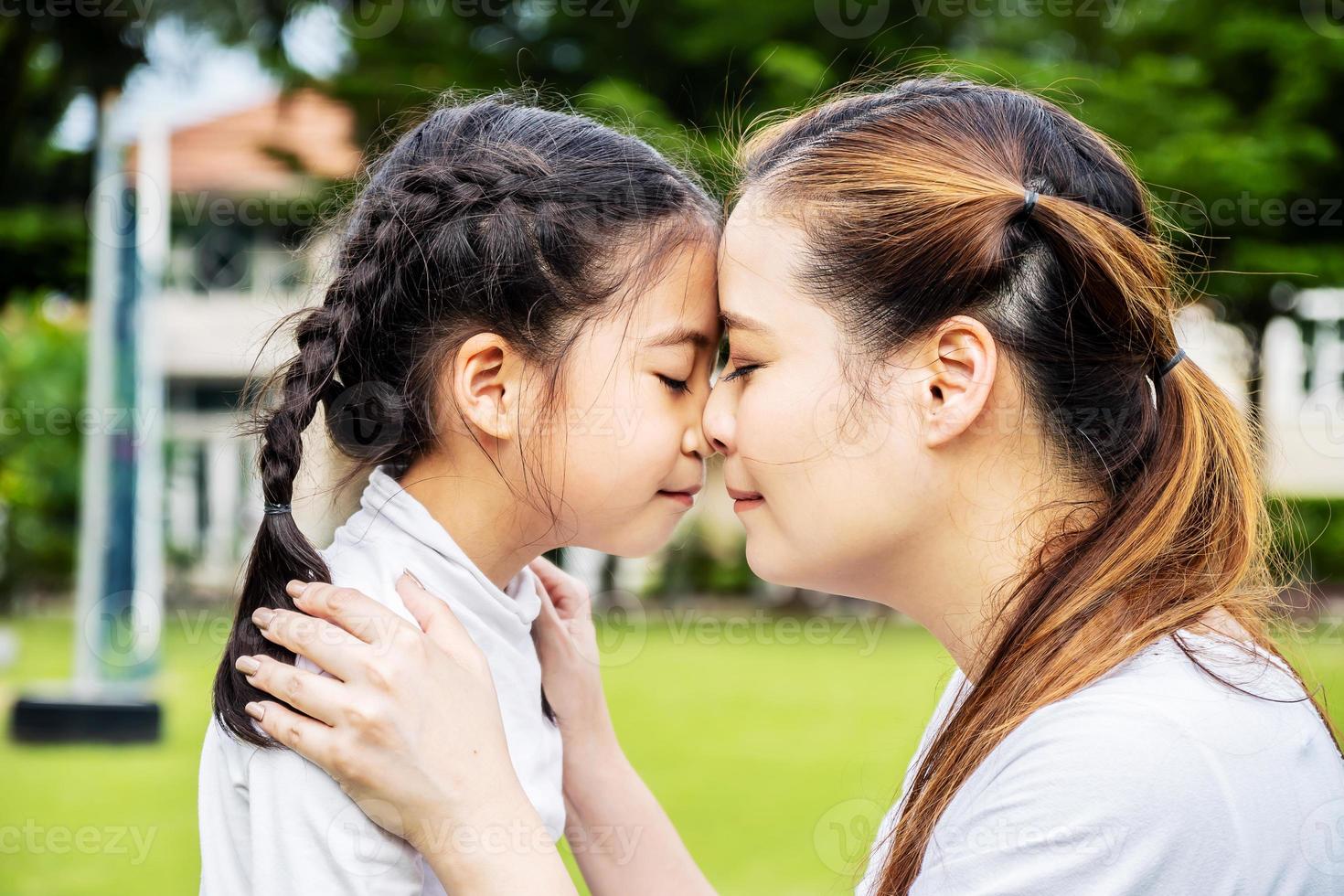 linda mãe asiática e filha abraçando e beijando no parque, conceito de união, família amorosa foto