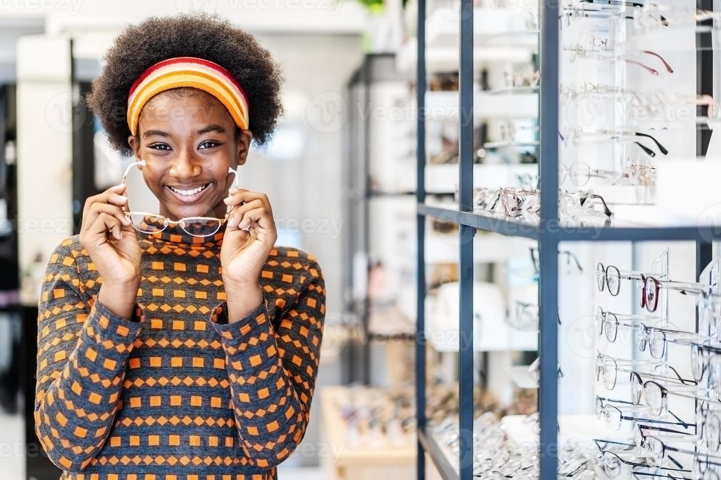 precisa de um óculos novo. jovem afro-americana na loja de óptica, escolhendo uma nova armação de óculos. médico, conceito de cuidados de saúde, usado para corrigir ou auxiliar a visão defeituosa foto